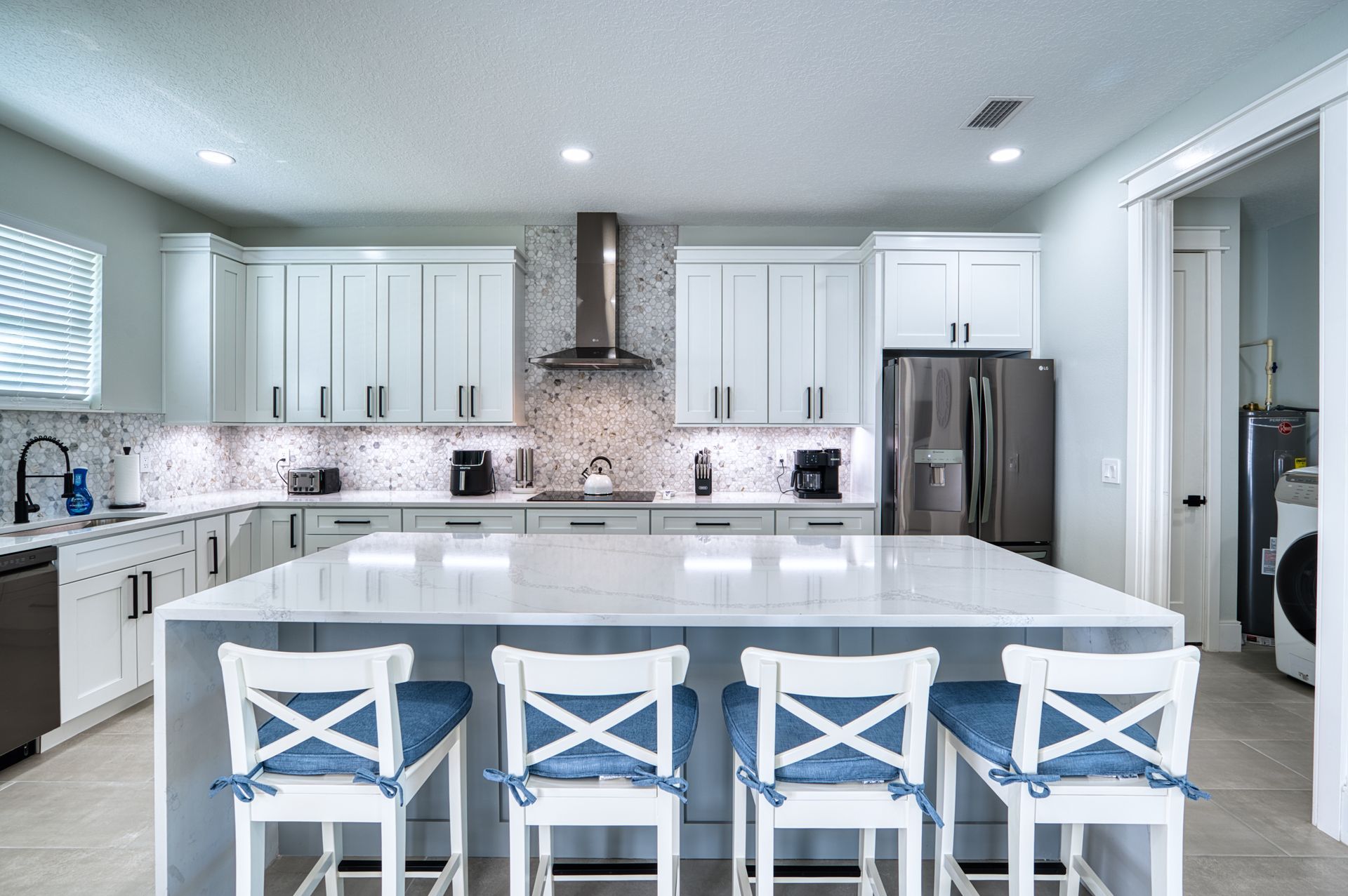Bright modern kitchen with white cabinets, marble island, and blue barstools