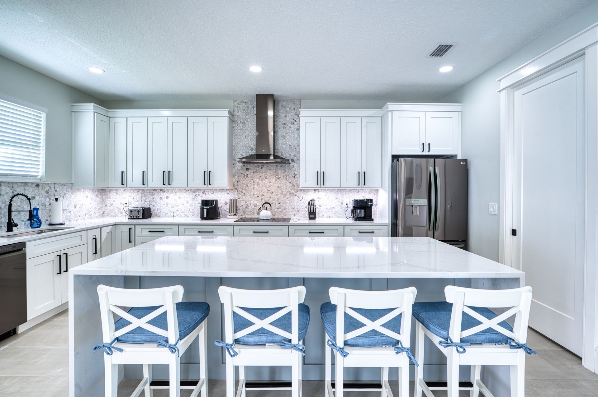 Bright white modern kitchen with a large island and four blue-and-white barstools.