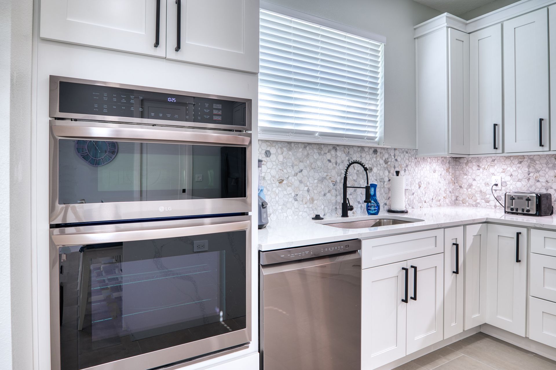 Bright modern kitchen with stainless steel oven, dishwasher, white cabinets, and marble backsplash