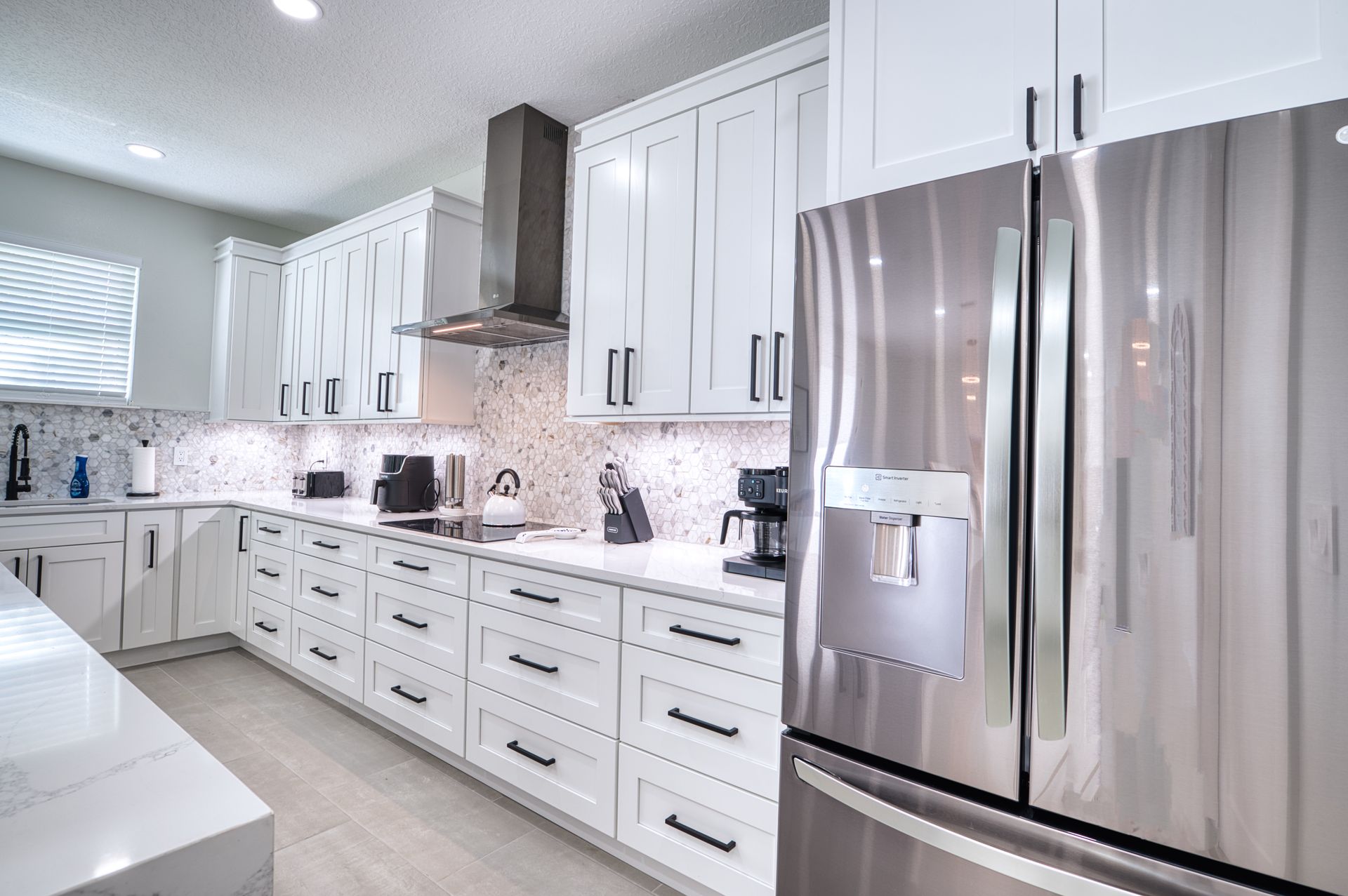 Bright white kitchen with stainless steel refrigerator, white cabinets, and marble-pattern backsplash