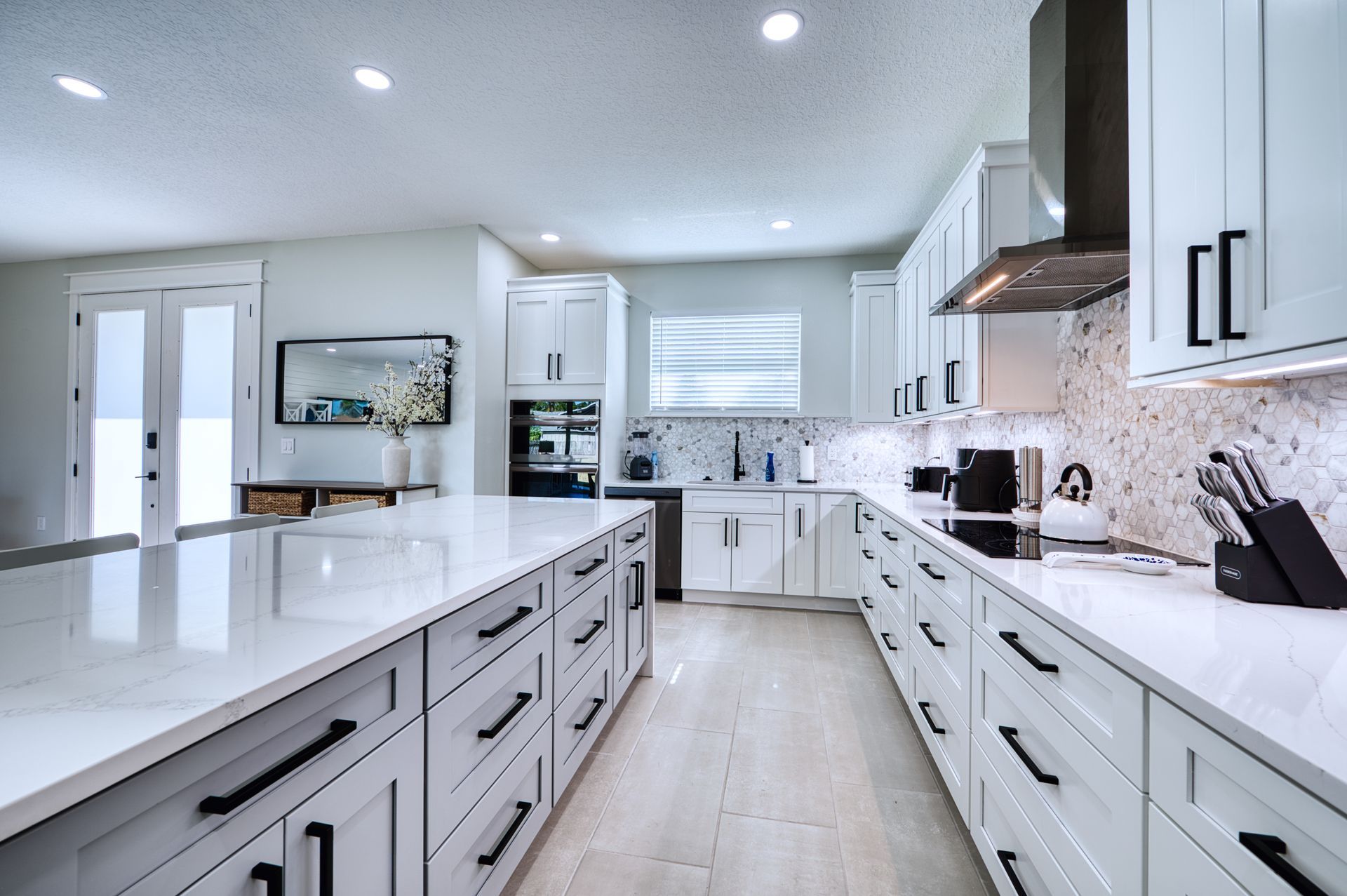Bright modern white kitchen with long countertops, island, stainless appliances, and light wood floors