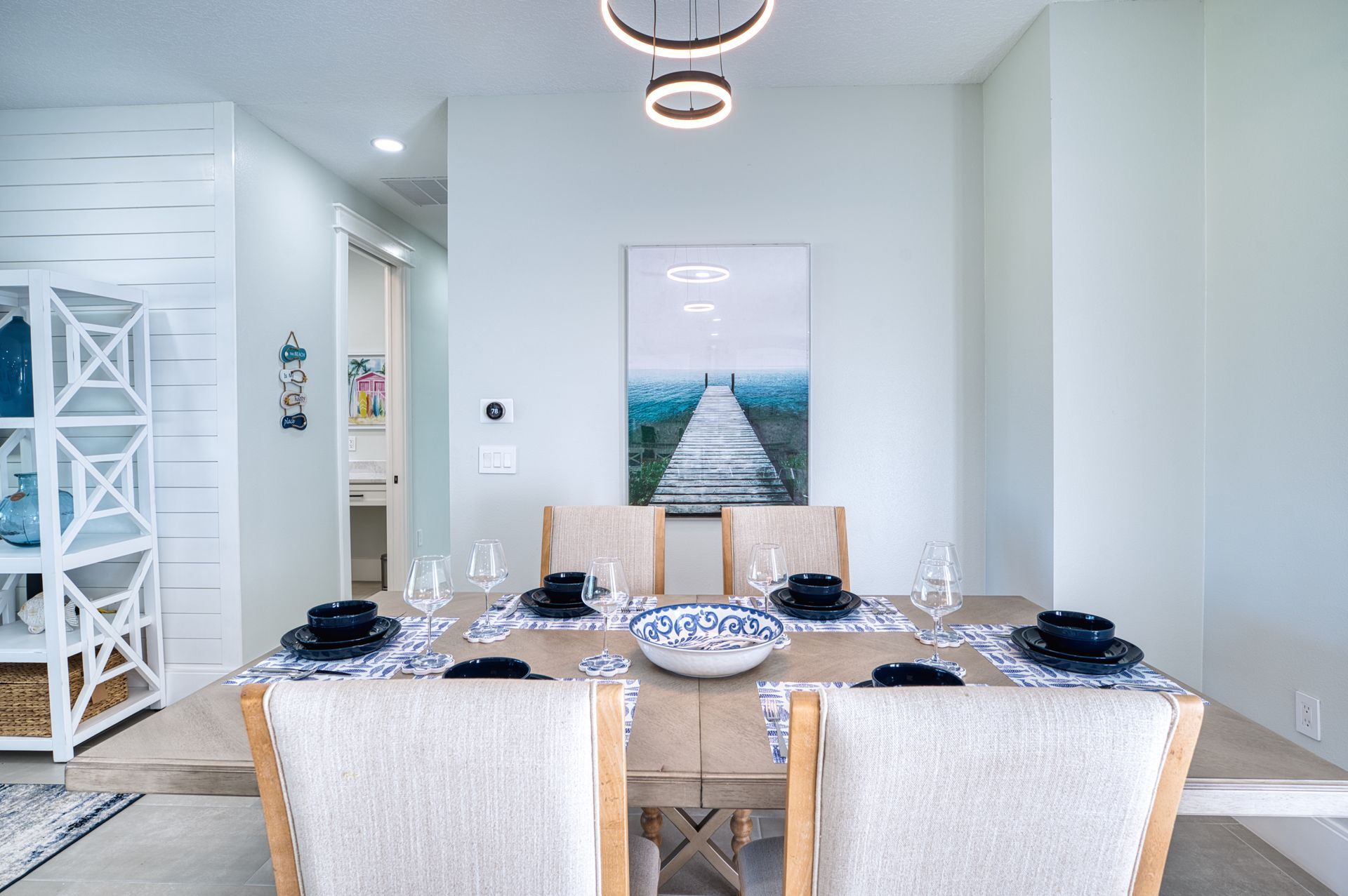 Bright dining room with a set table, white chairs, and a beach pier wall print