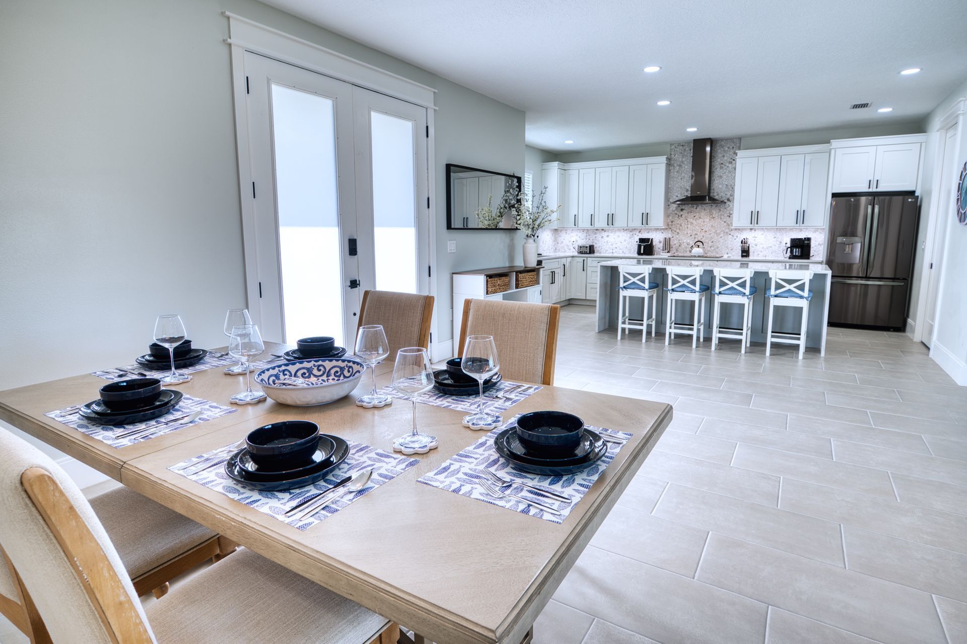Bright open kitchen and dining area with a set dining table, island stools, and white cabinets.
