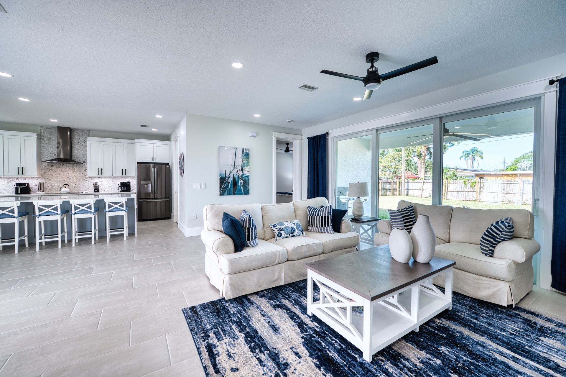 Bright open living room with white sofas, navy rug, coffee table, and kitchen bar in background