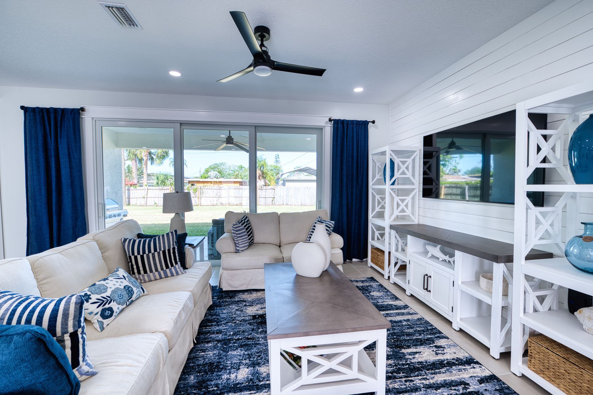 Bright living room with blue accents, white sofas, large windows, and TV console