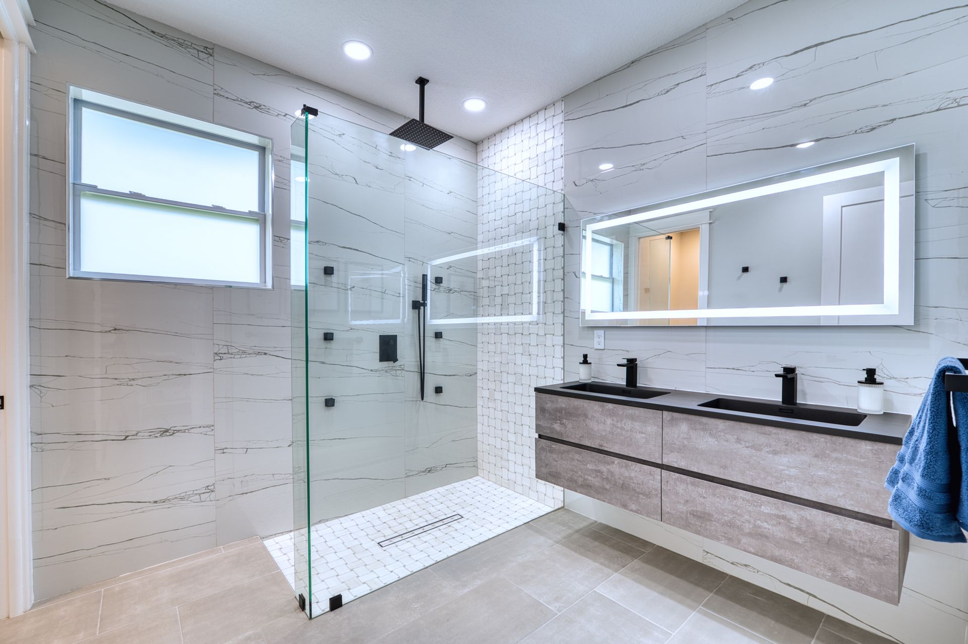 Modern bathroom with glass shower, double vanity, and large illuminated mirror.