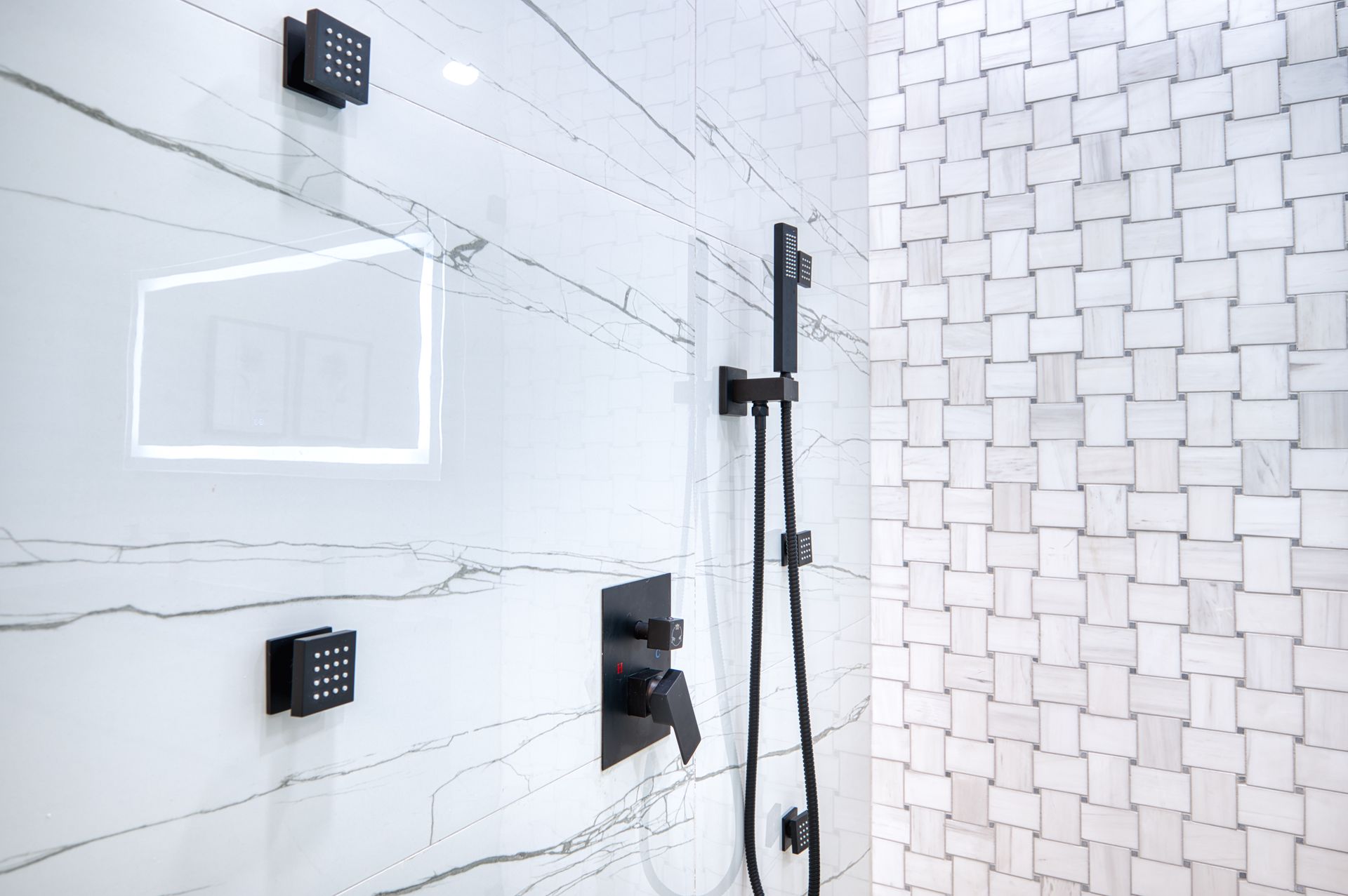 Modern bathroom shower with white tile, glass partition, black fixtures, and rain showerhead