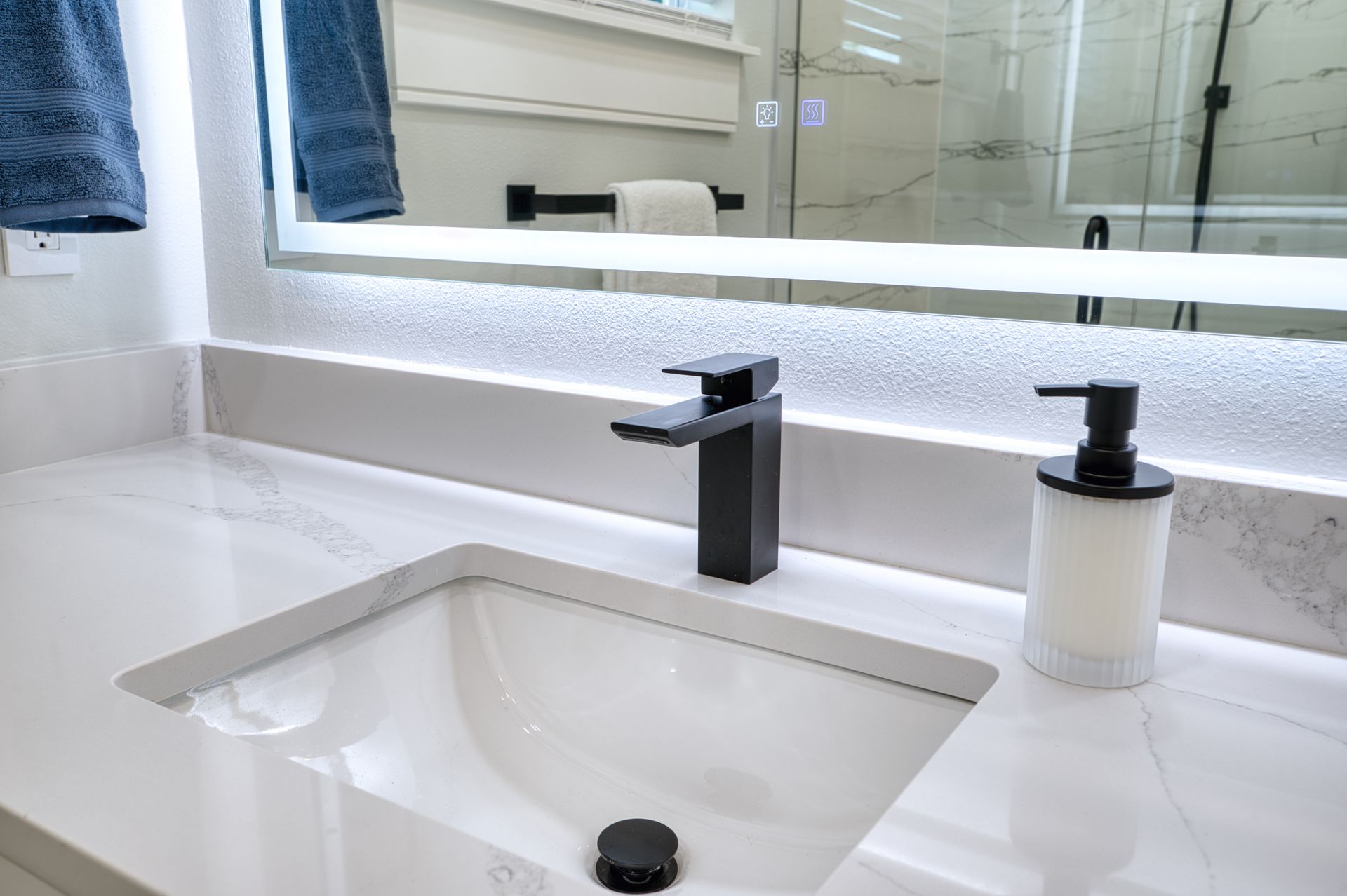 Modern white bathroom vanity with sink, black faucet, and illuminated mirror
