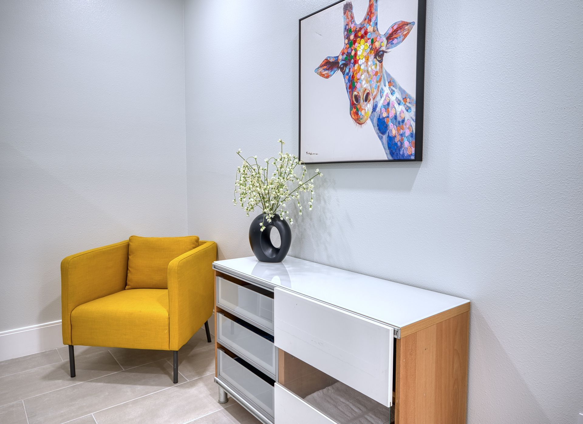Modern room with a mustard armchair, white console table, vase of flowers, and colorful giraffe artwork.