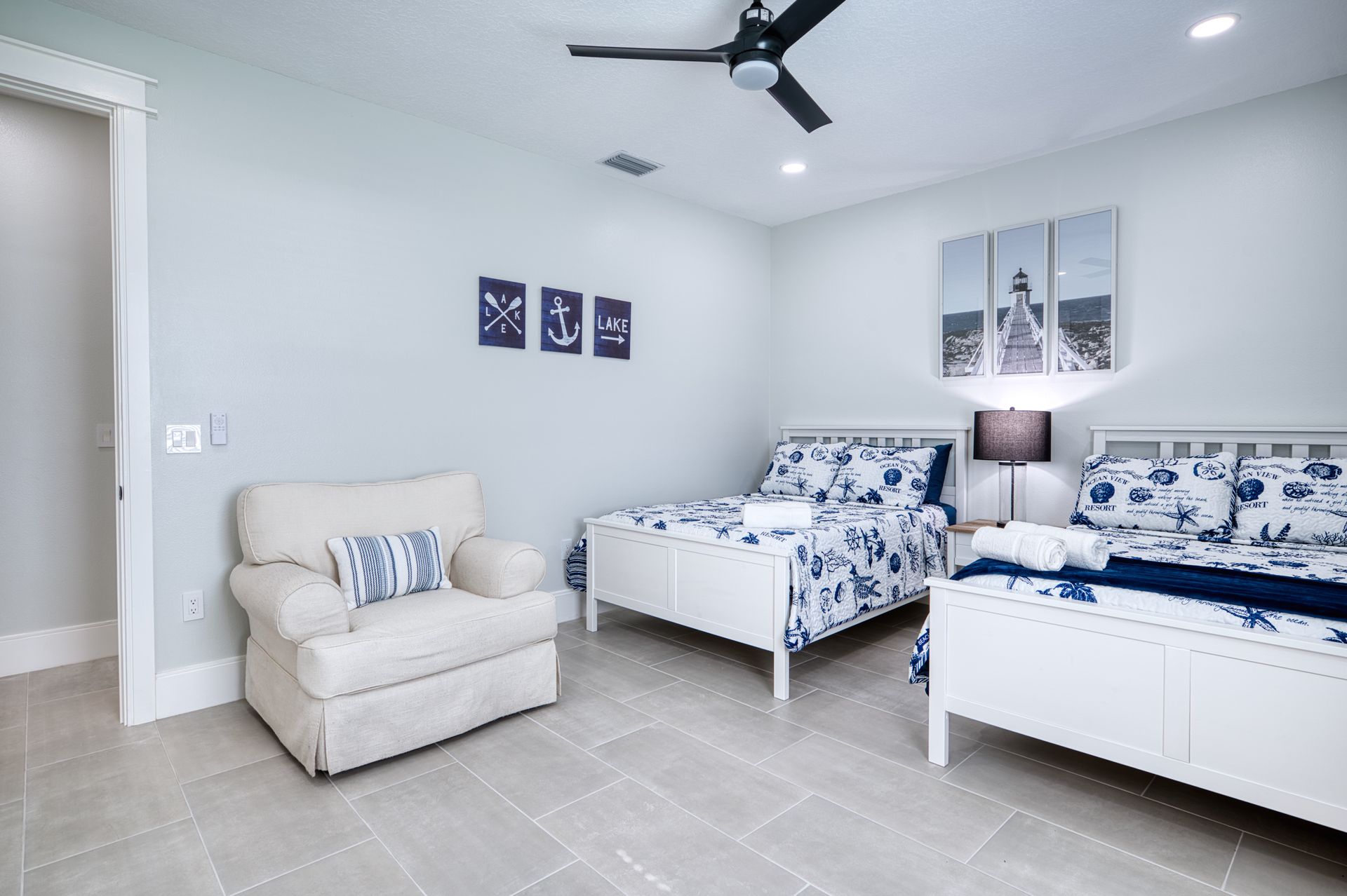 Bright bedroom with two twin beds, beige armchair, blue decor, and a ceiling fan