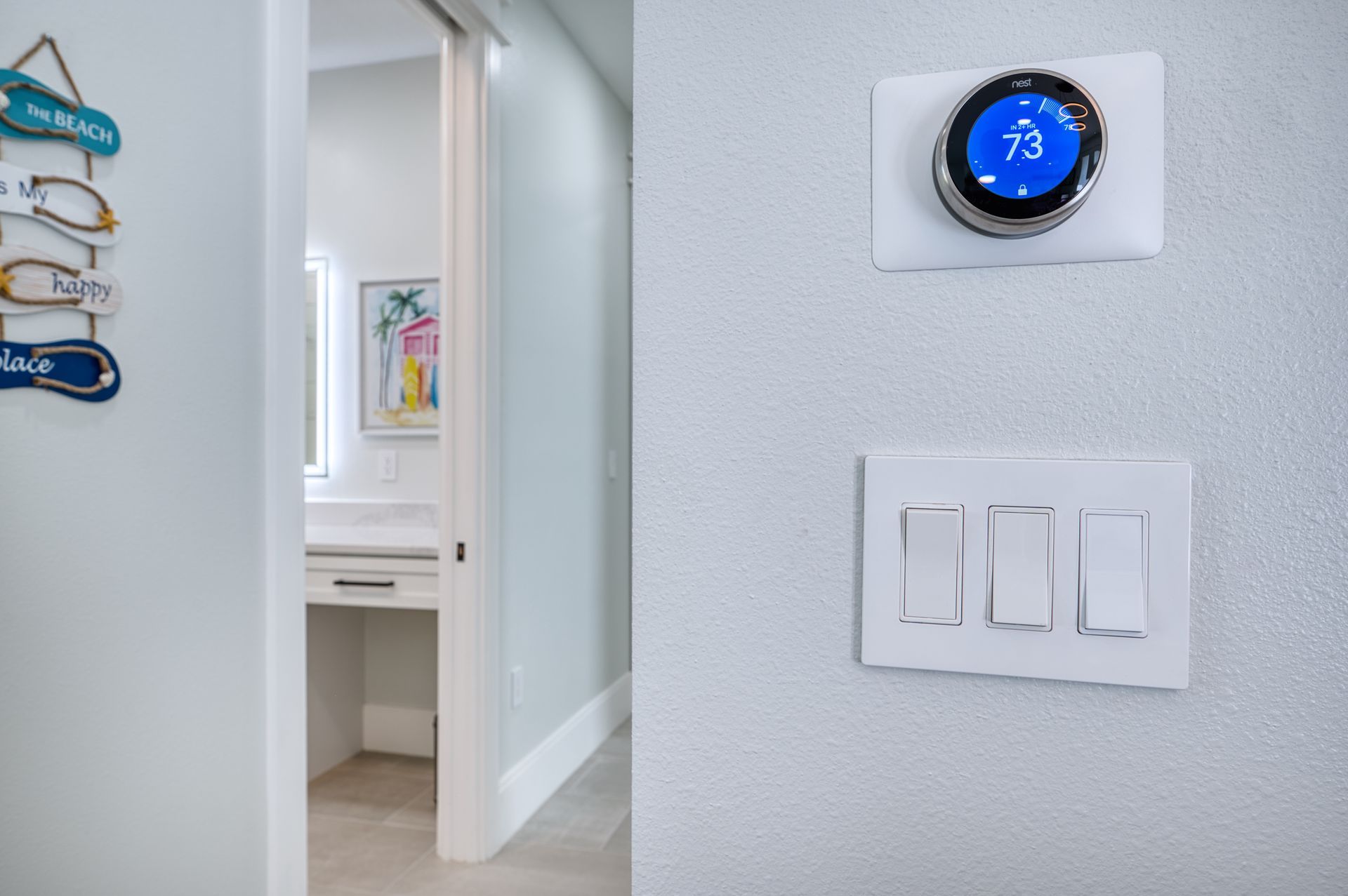Hallway with white walls, thermostat showing 73°, and a three-switch light panel