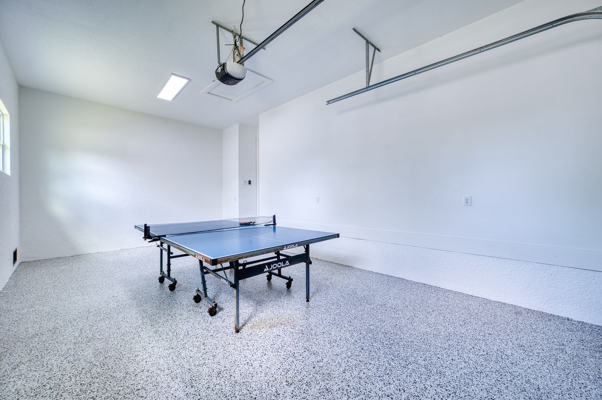 Bright garage with a ping-pong table on a speckled floor and overhead storage racks