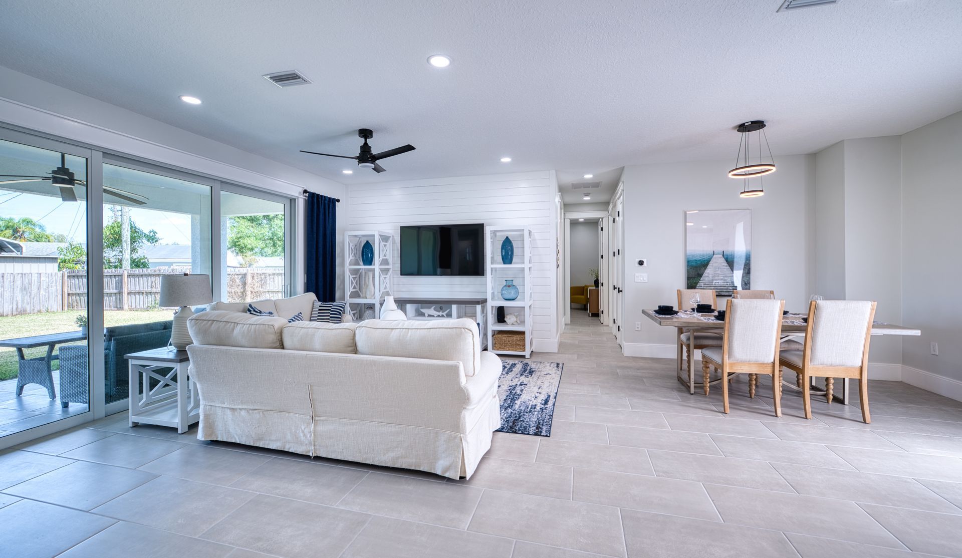Bright open-plan living and dining room with white sofa, wood table, large windows, and patio access
