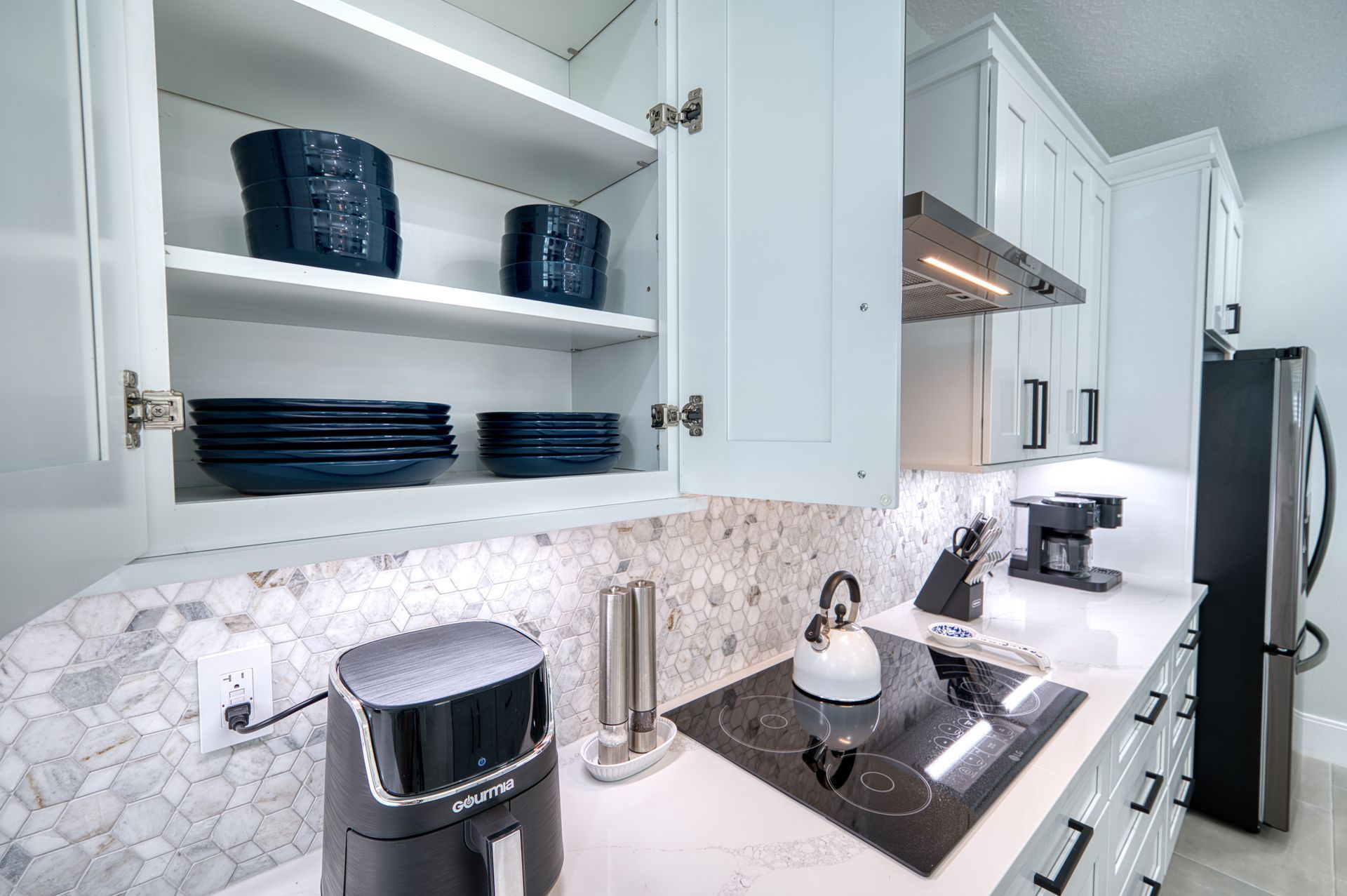 Bright white kitchen with open shelves, dark dishes, a sink, and a coffee maker on a black countertop.