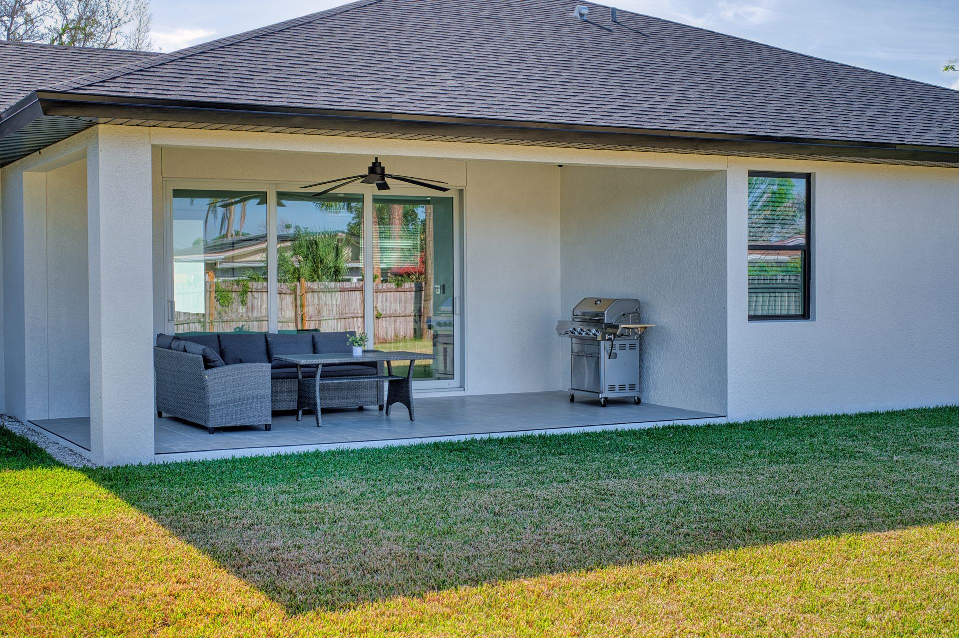 Covered patio with outdoor sofa, grill, and sliding glass doors beside a grassy yard