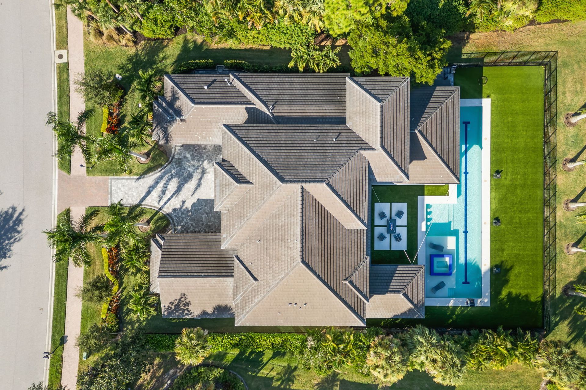 Aerial view of a house with a backyard pool, surrounded by lush greenery and a driveway.