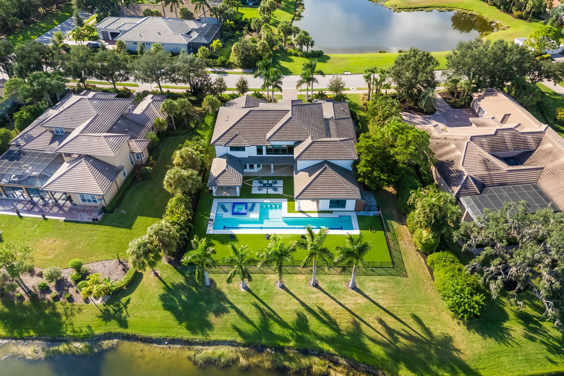 Aerial view of three luxury homes with pools and a lake in the background