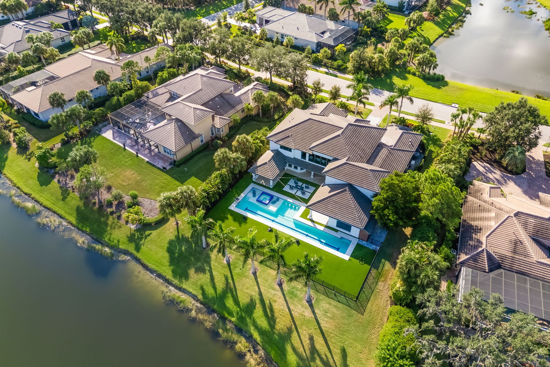 Aerial view of lakeside luxury homes with a turquoise pool and lush green landscaping
