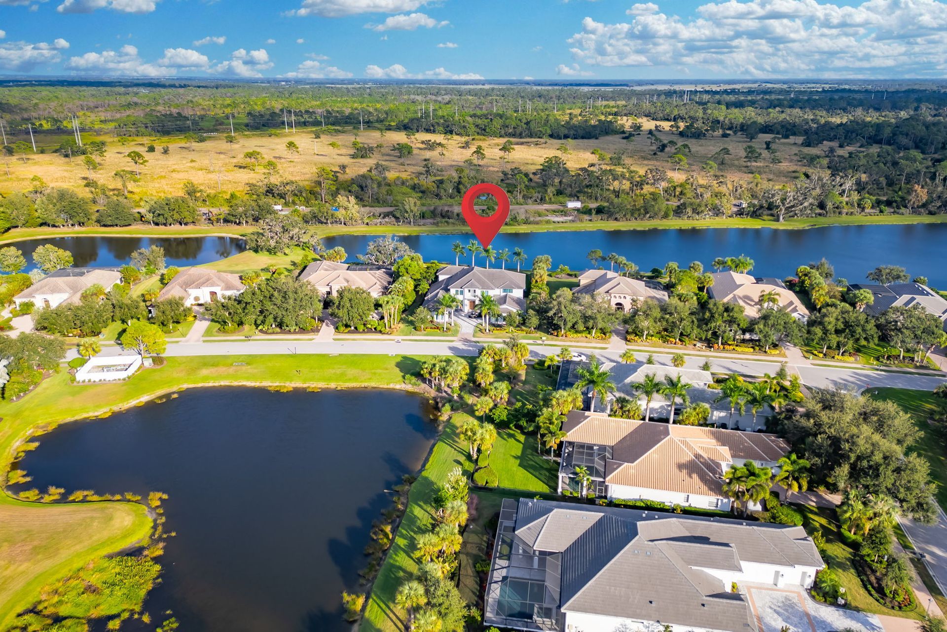 Aerial view of a lakeside neighborhood with homes, trees, and a river or canal under a clear sky.