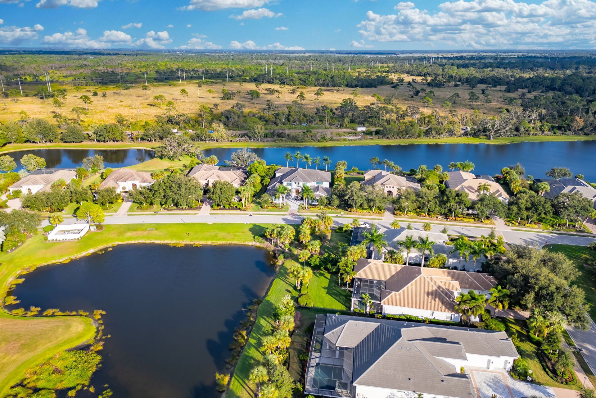 Aerial view of a lakeside neighborhood with homes, a river, and green fields under a blue sky