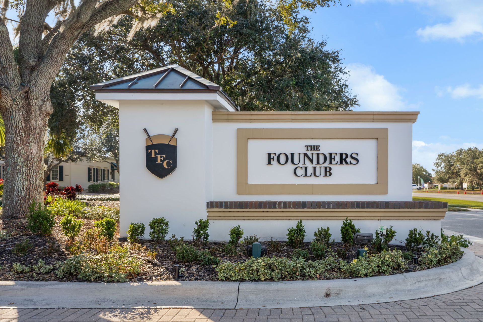 Entrance sign for The Founders Club on a landscaped roadside, with white and tan stone pillars.