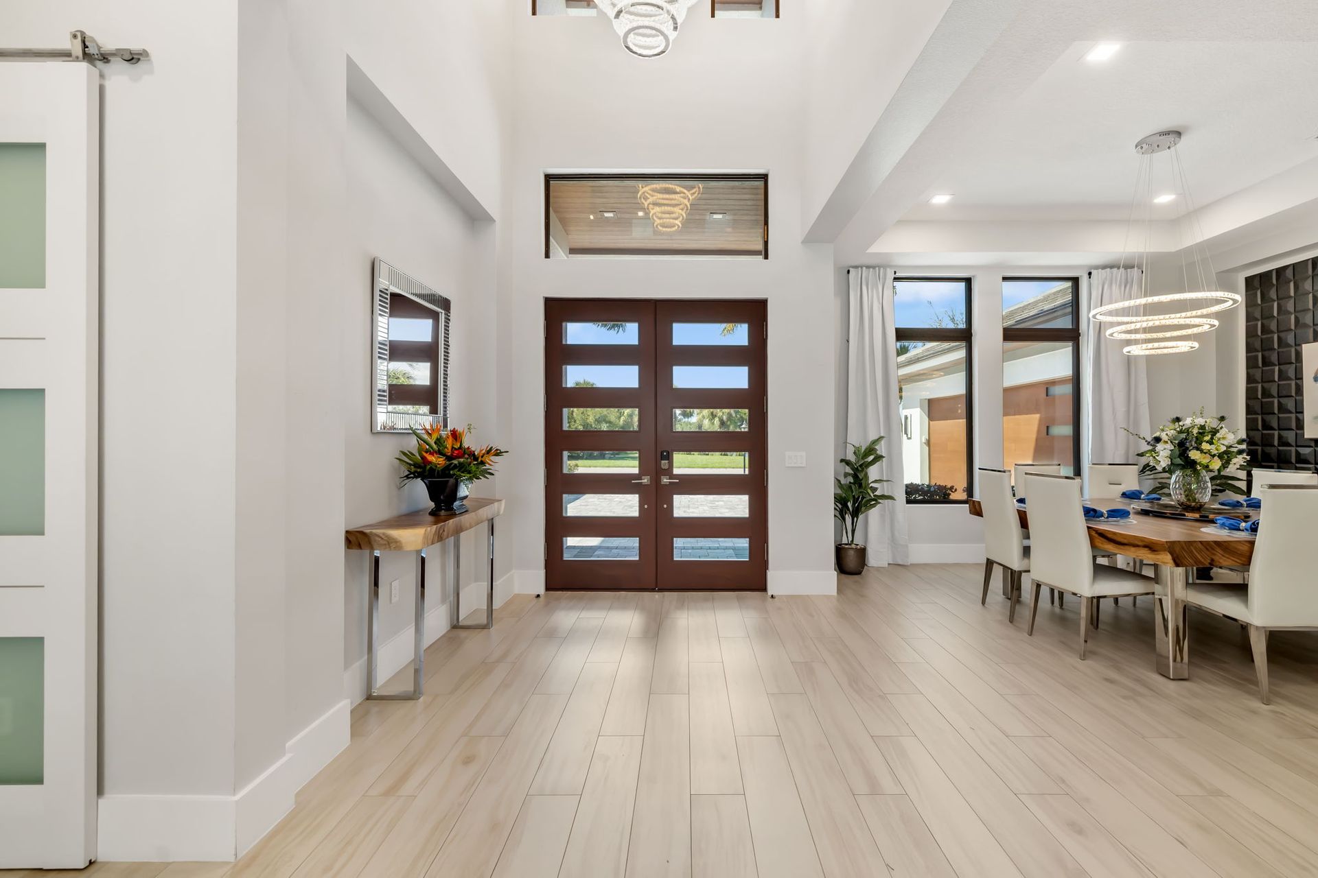 Bright entry hall with white walls, wood floor, front door, and console tables with flowers.