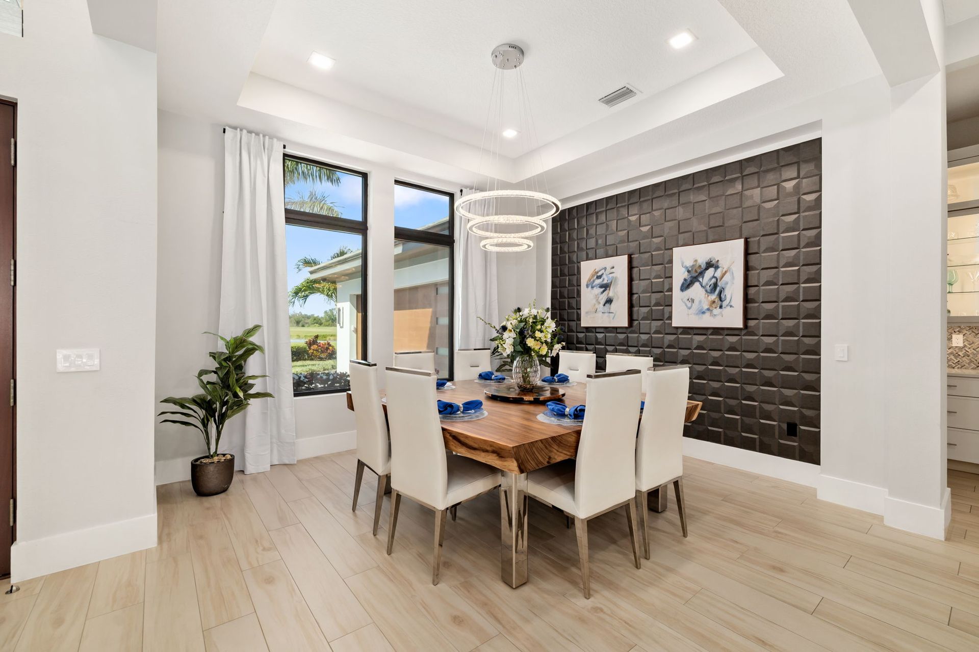 Bright dining room with wood table, white chairs, black accent wall, and large windows.