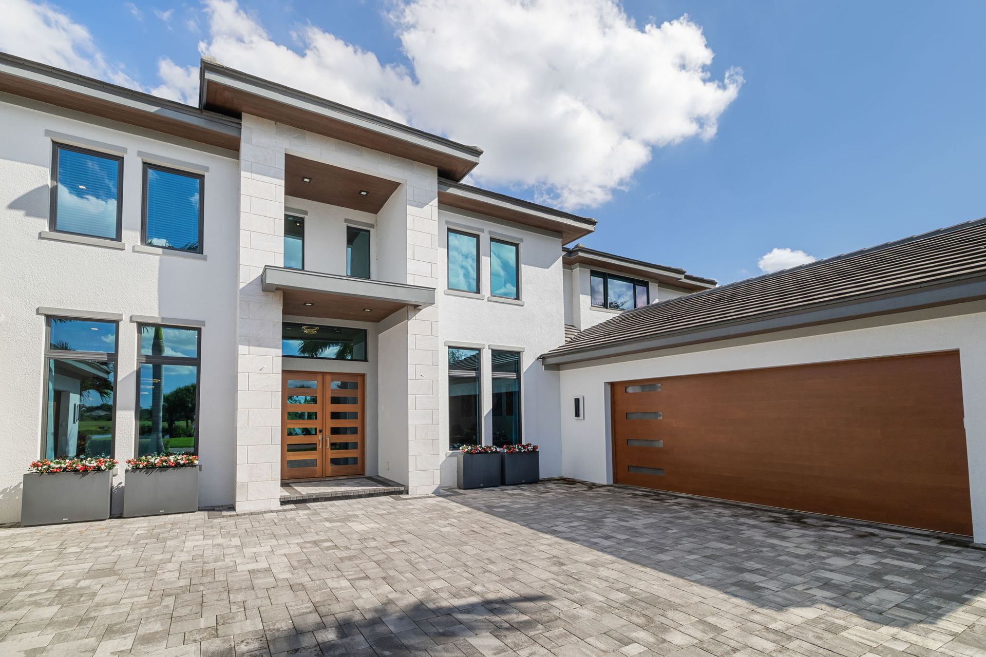Modern two-story house with white walls, blue-trimmed windows, and a large brown garage door under a bright sky