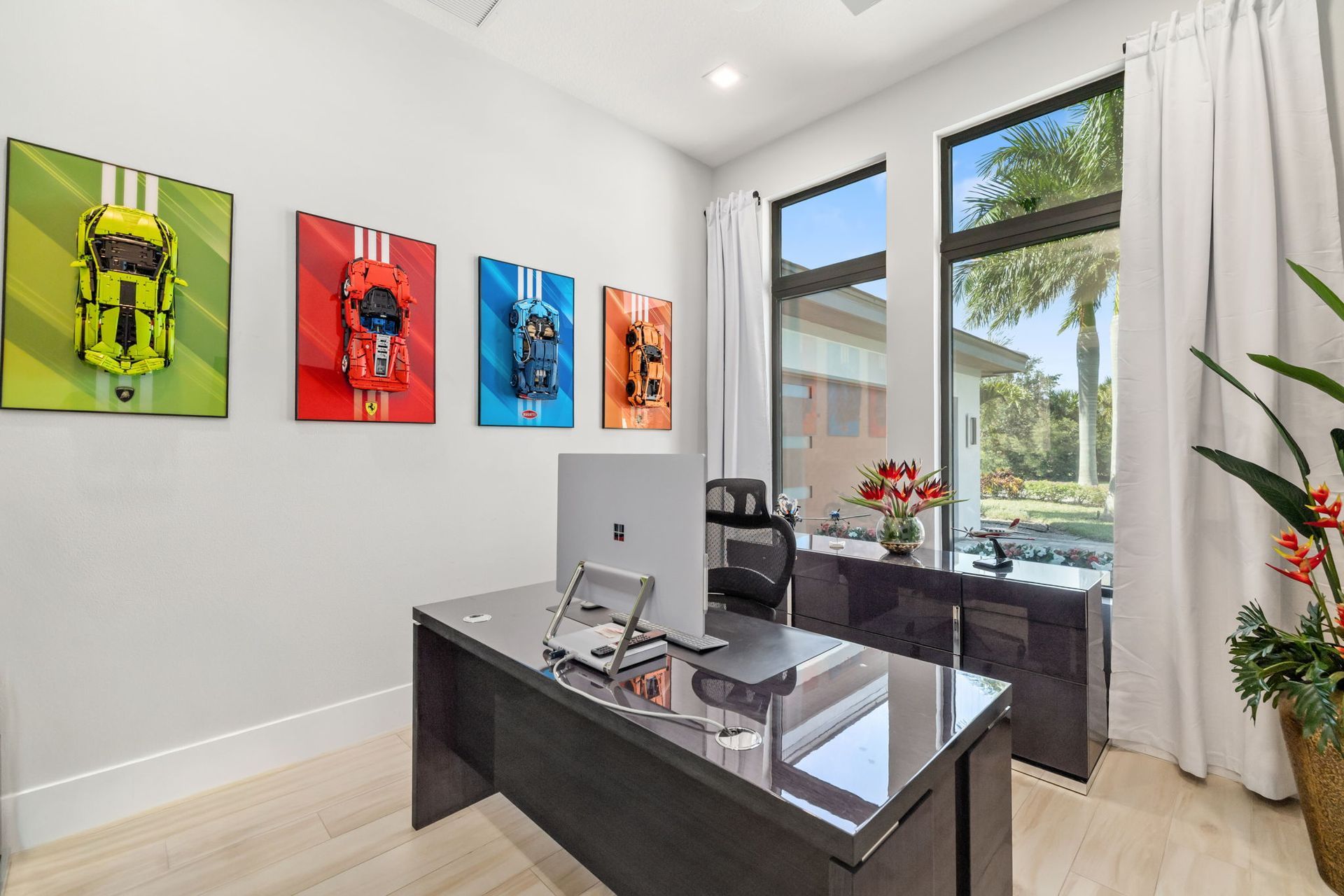 Modern home office with glass desk, colorful wall art, and large window overlooking greenery