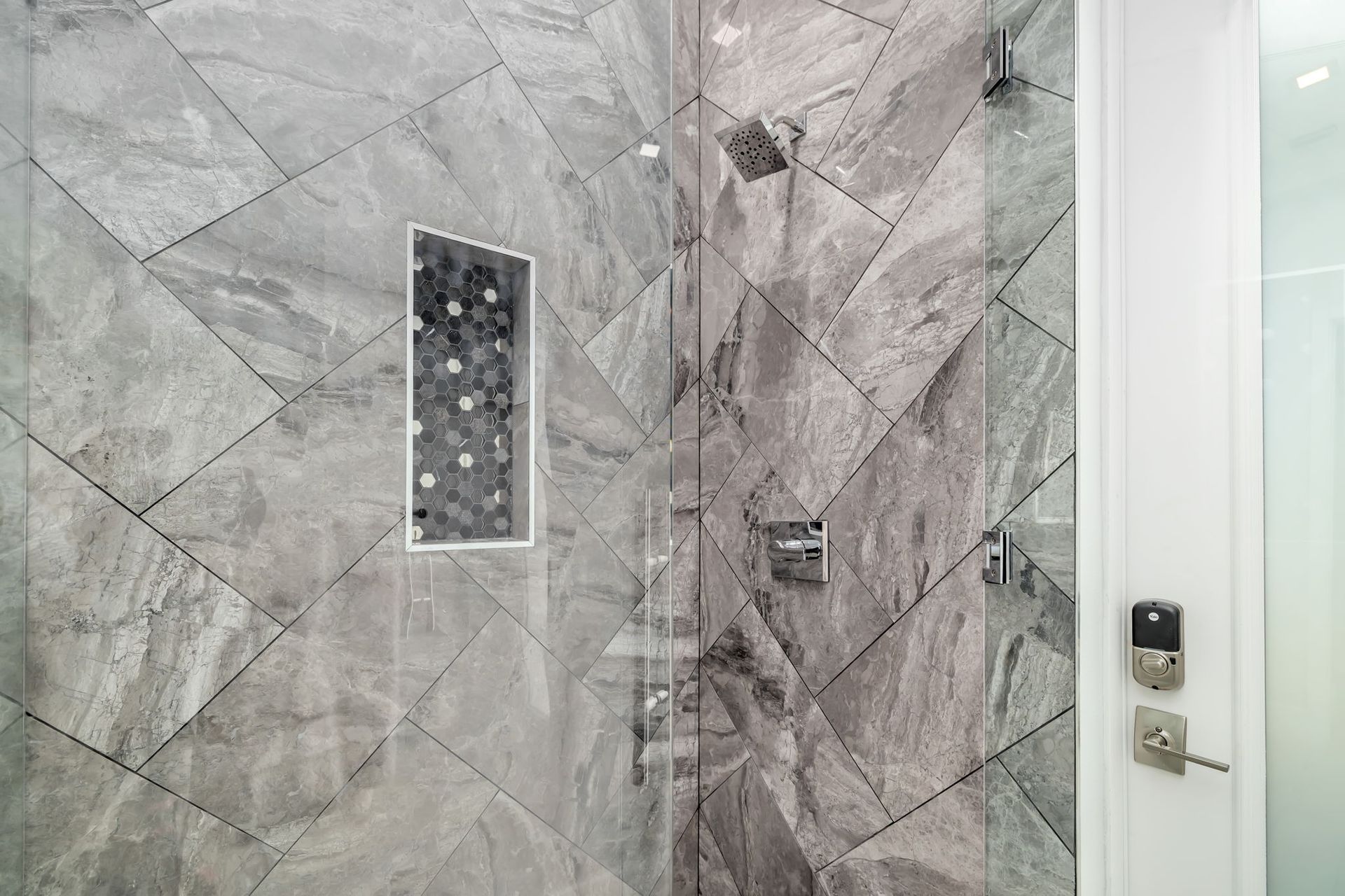 Modern bathroom shower with gray marble tile, built-in niche, and chrome fixtures