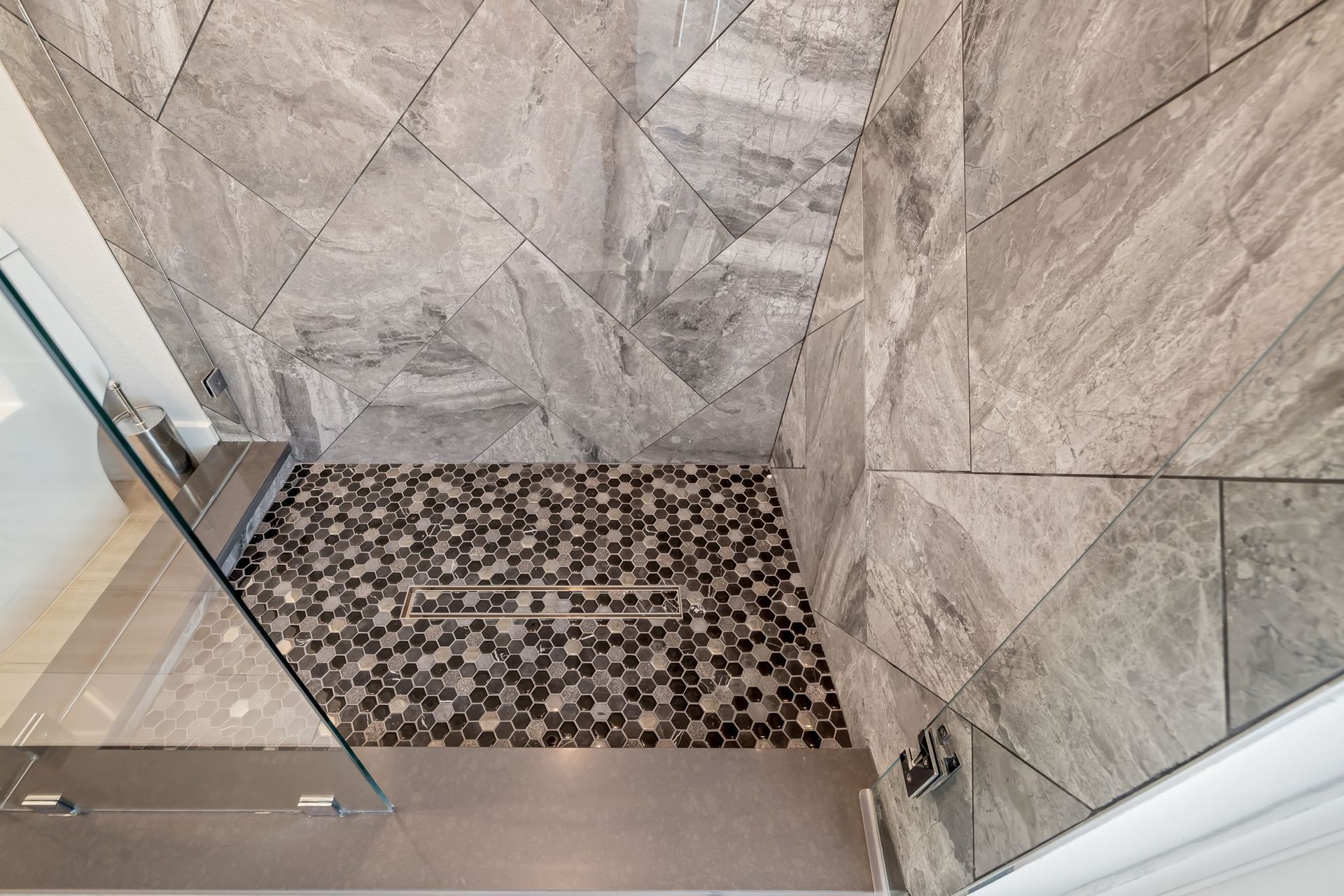 Corner shower with gray tile walls and a pebble mosaic floor drain area