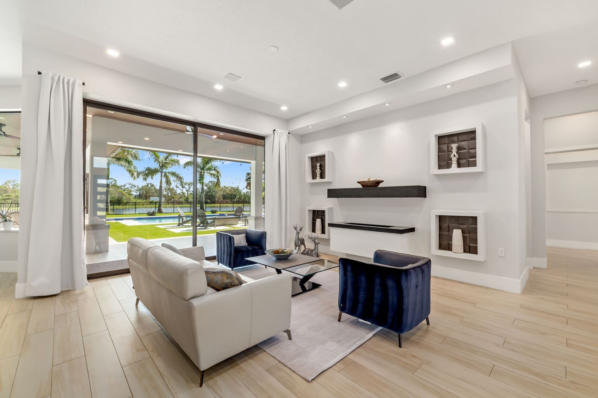 Bright modern living room with white sofas, fireplace, and large sliding doors to a pool and palm view