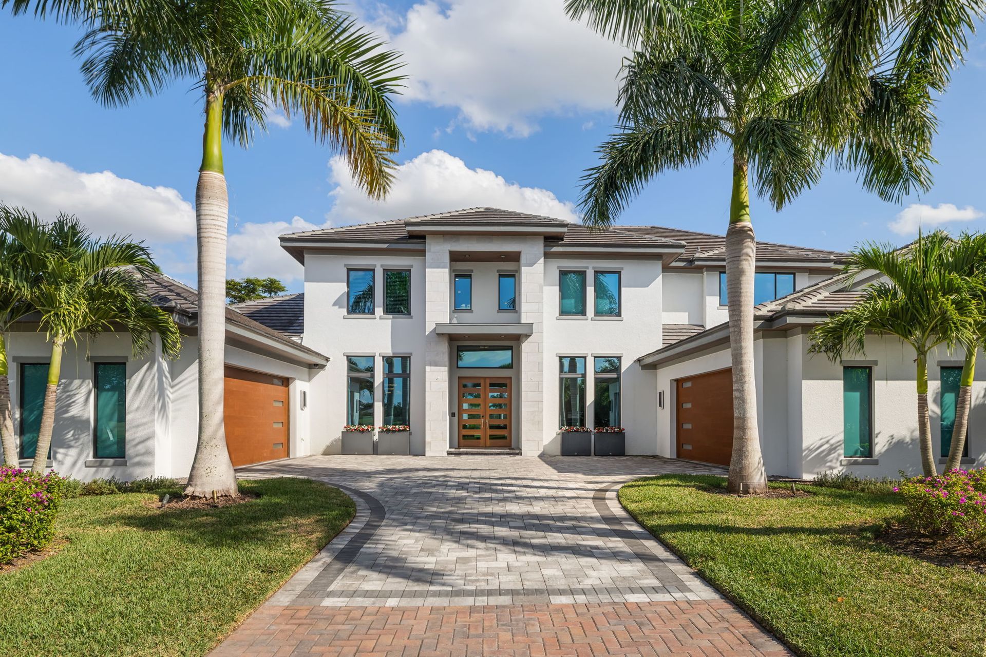 Modern white two-story mansion with palm trees, paved driveway, and symmetrical garage wings