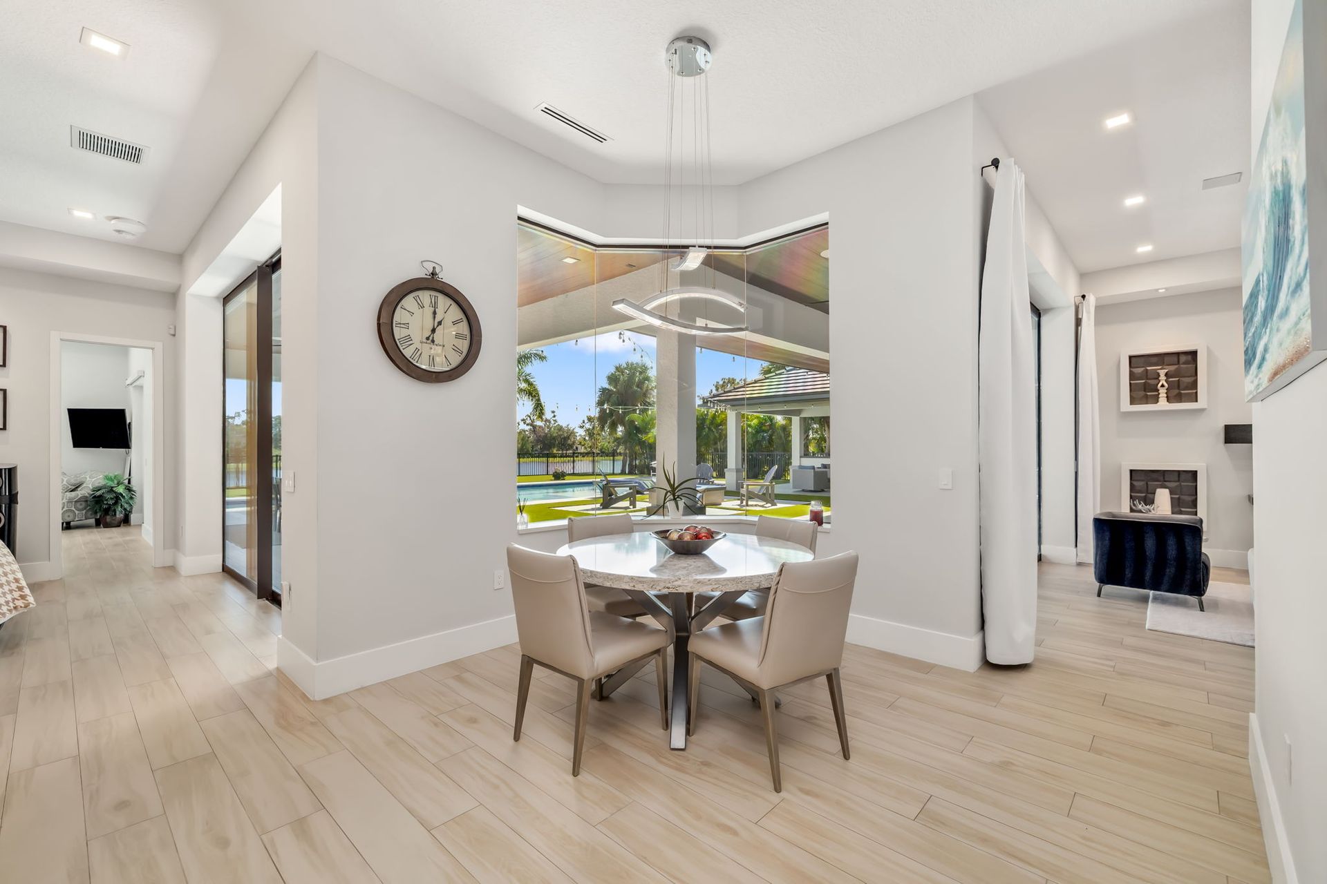 Bright dining area with white chairs, large window, and view of a sunny patio and pool