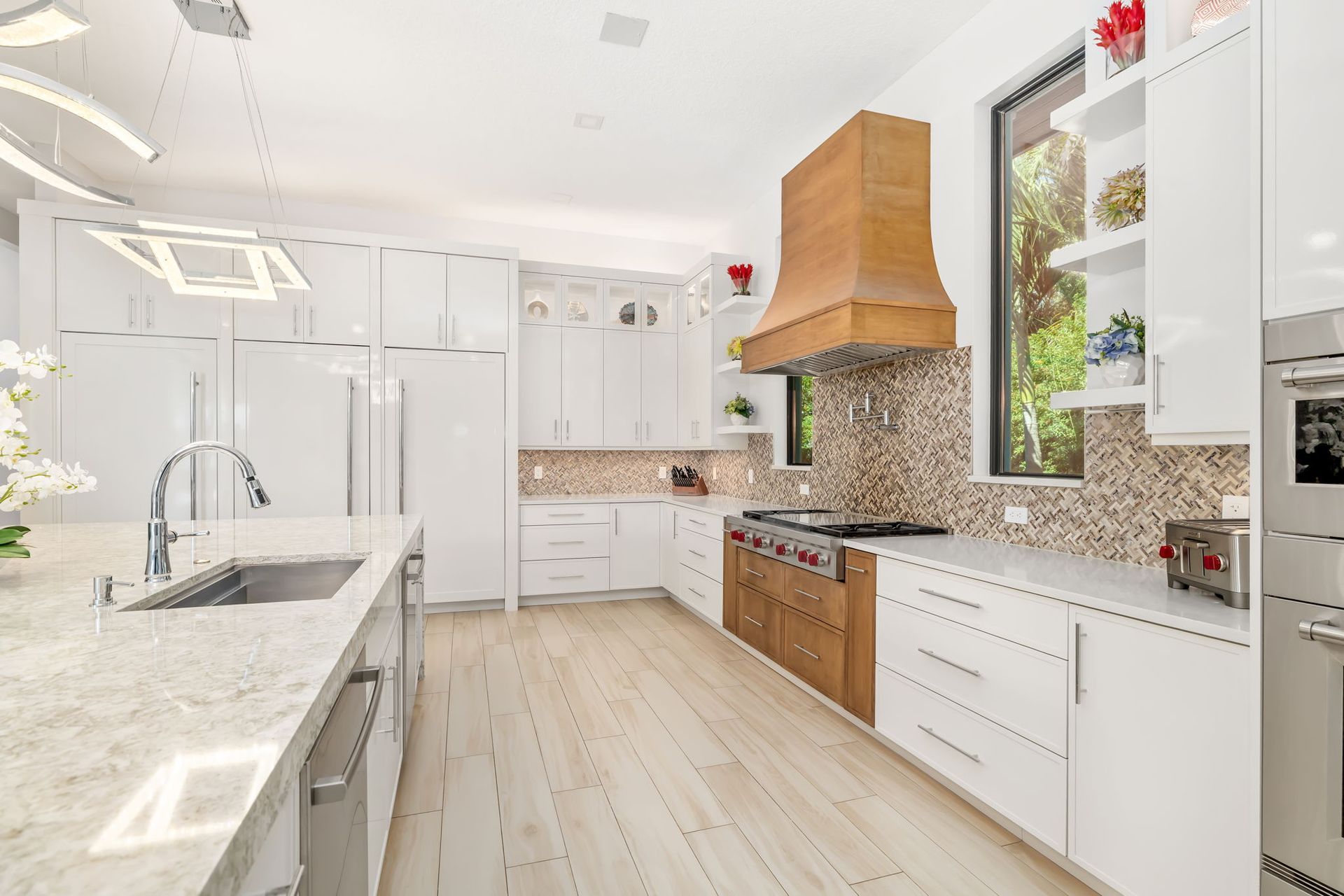 Bright modern kitchen with white cabinets, wooden range hood, granite counters, and light wood floor