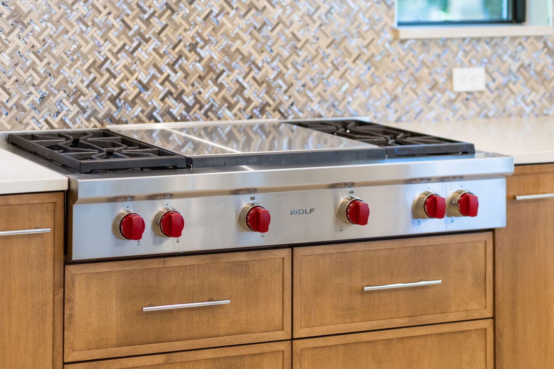 Stainless steel gas cooktop with red knobs built into a wooden kitchen counter.