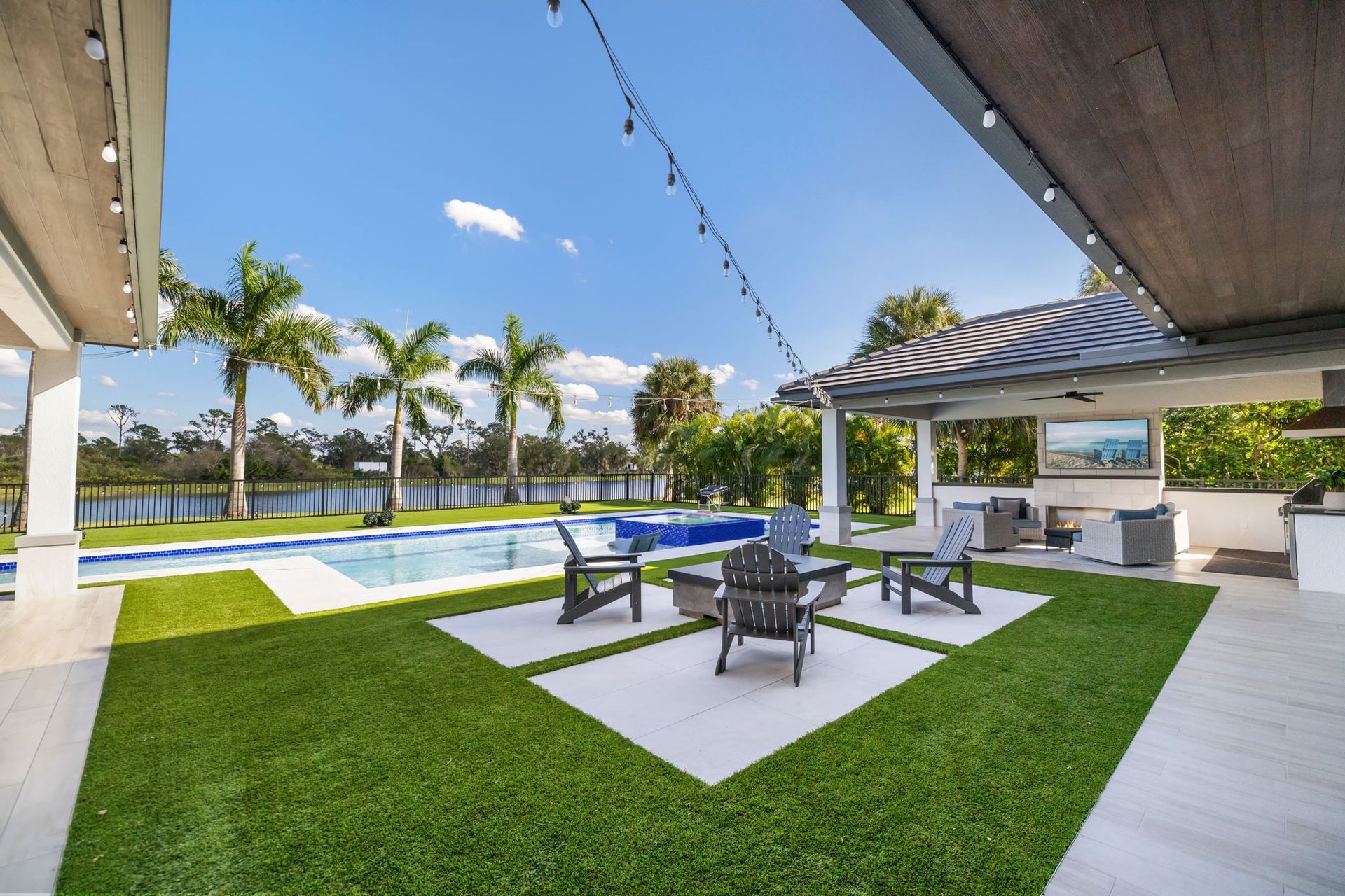 Modern patio with lounge chairs, white seating, palm trees, pool, and blue sky view