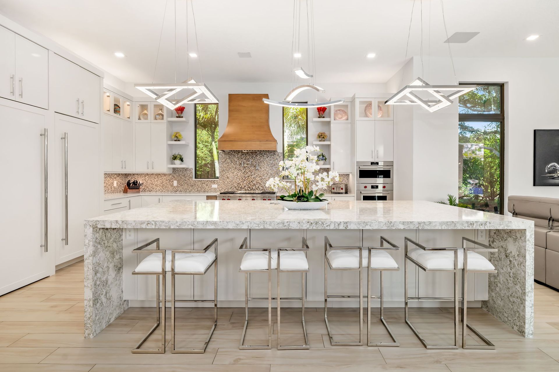 Bright modern kitchen with white cabinets, marble island, bar stools, and hanging pendant lights