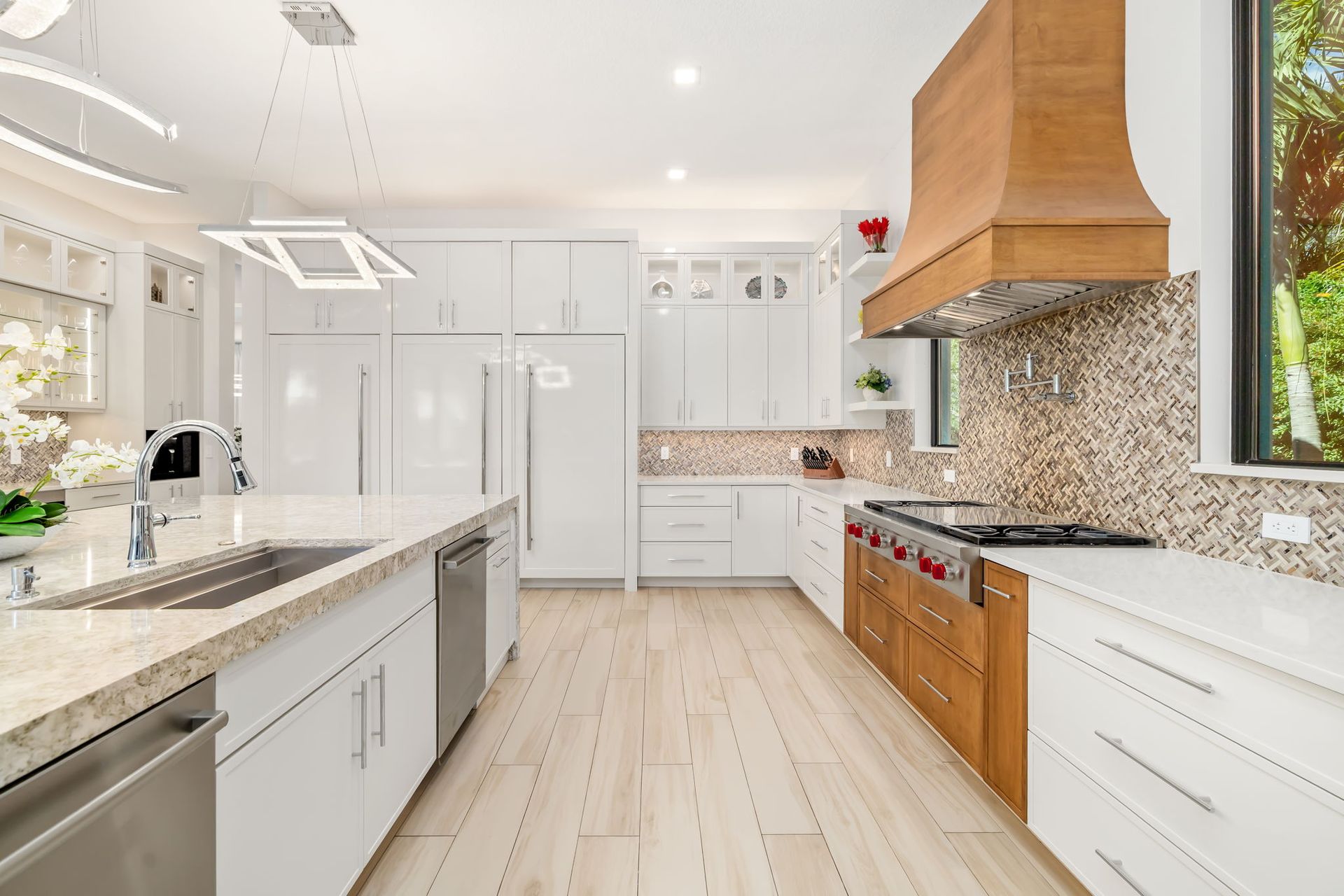 Bright modern kitchen with white cabinets, marble countertops, wood accents, and stainless appliances