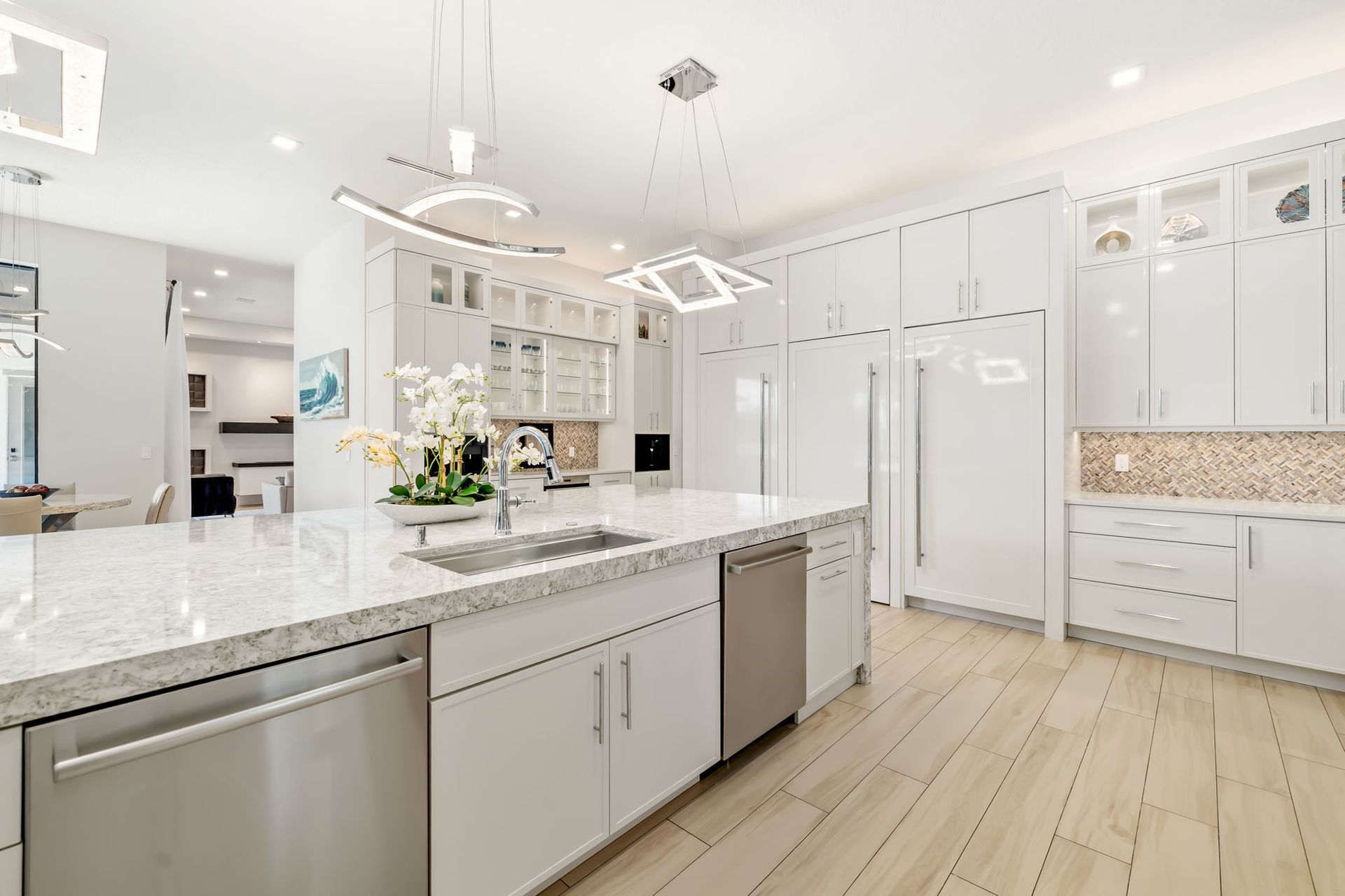 Bright modern kitchen with white cabinets, marble island, stainless appliances, and light wood floors