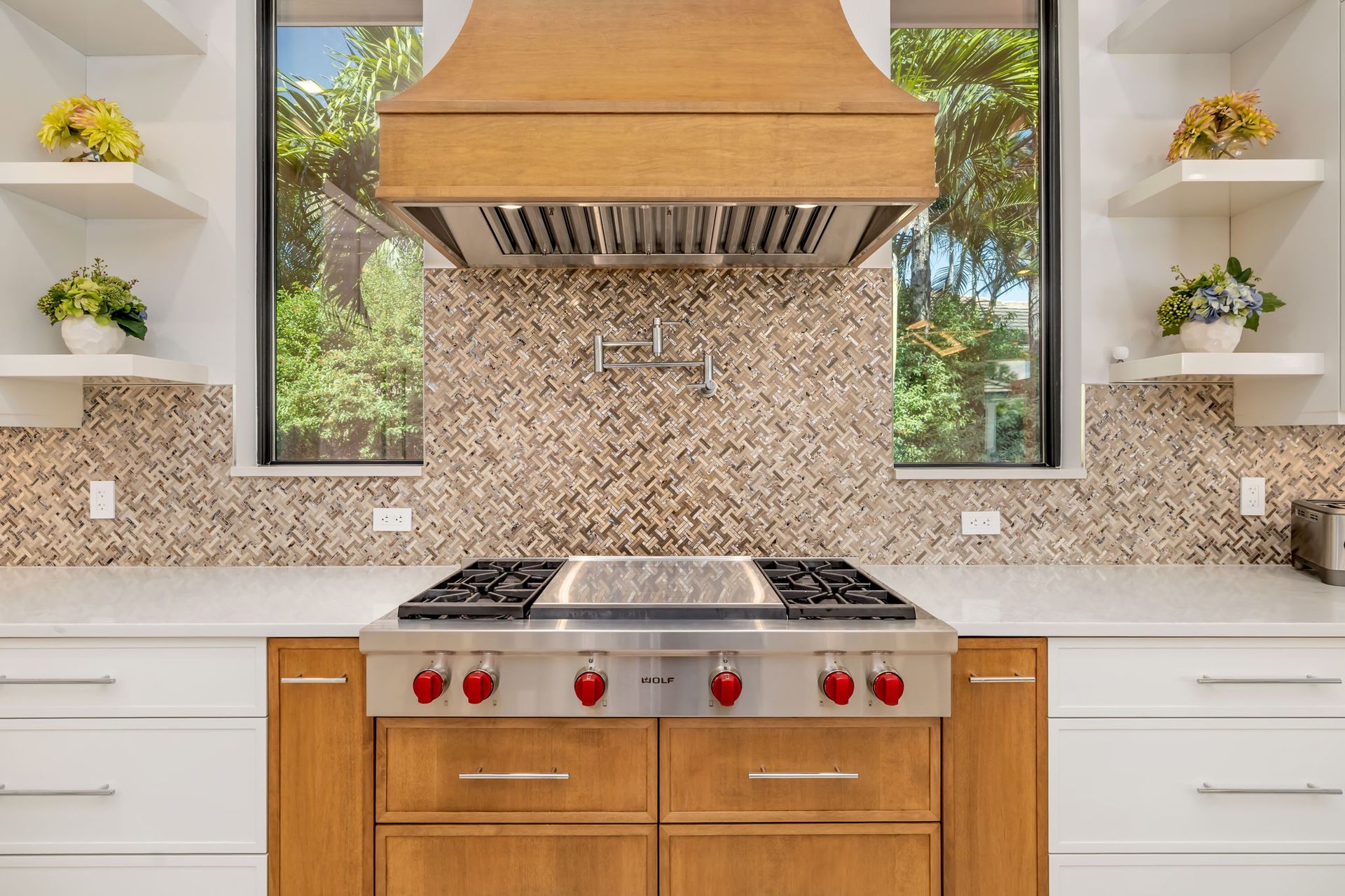Modern kitchen with wood cabinets, mosaic backsplash, stainless range, and pendant hood between two windows