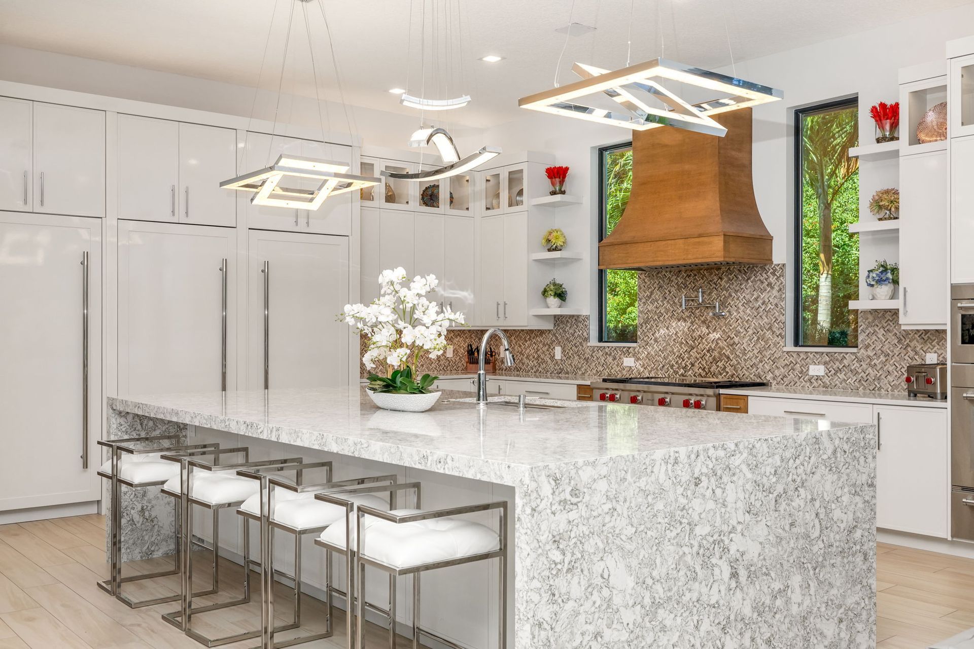 Bright modern kitchen with white island, bar stools, pendant lights, and copper range hood