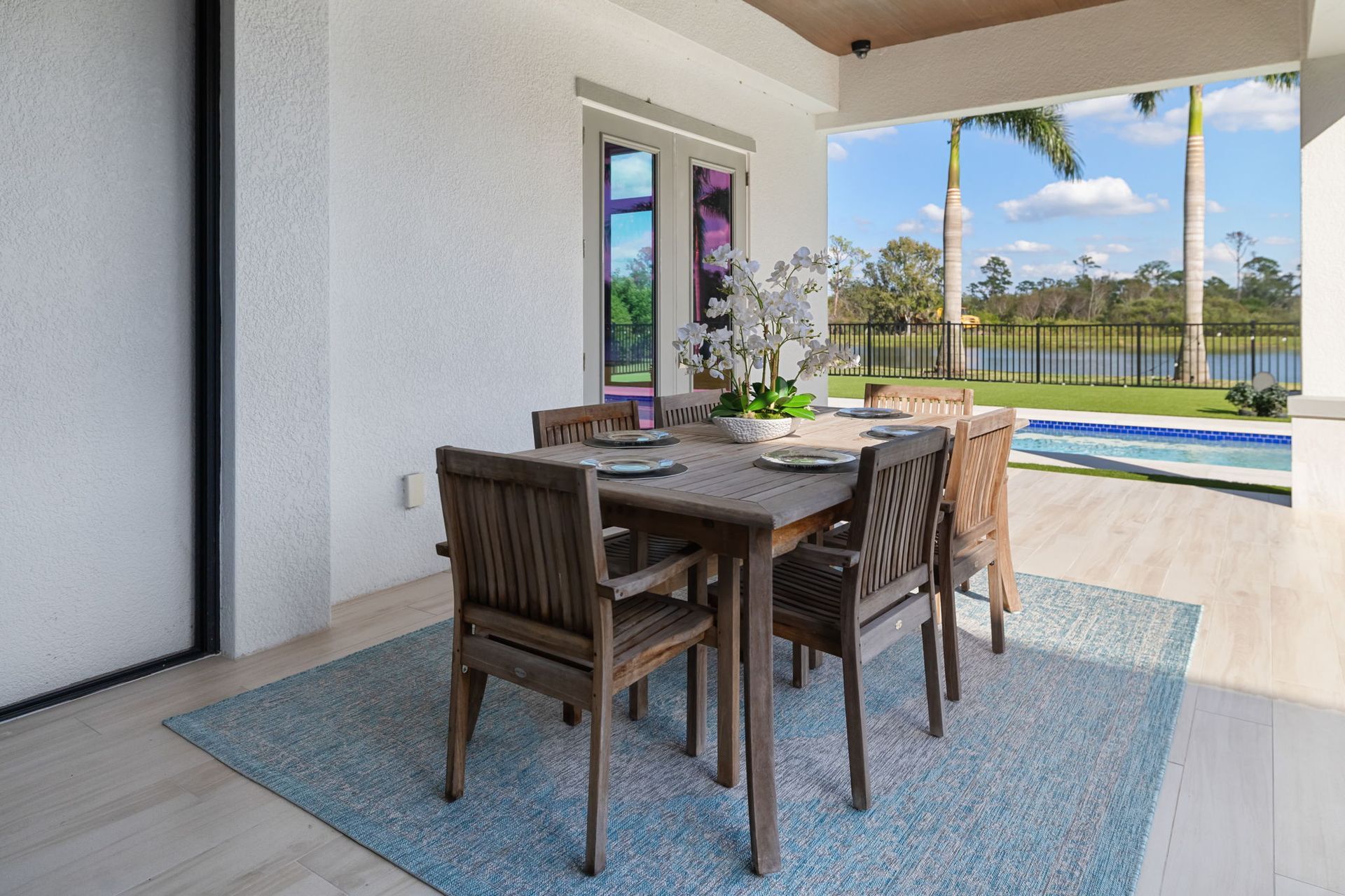 Outdoor dining table on a covered patio overlooking a pool and palm trees