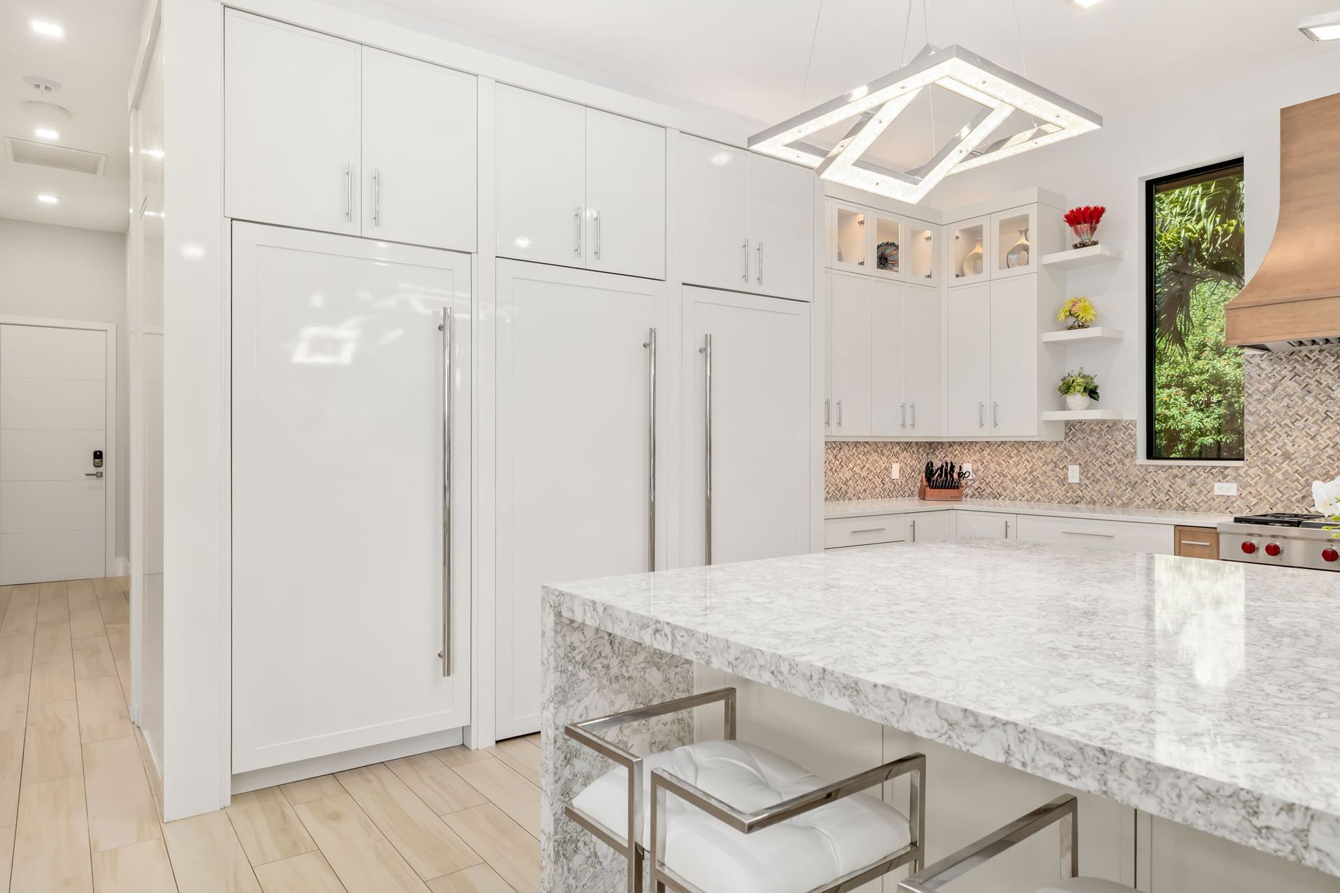 Modern white kitchen with marble island, stainless appliances, and light wood flooring