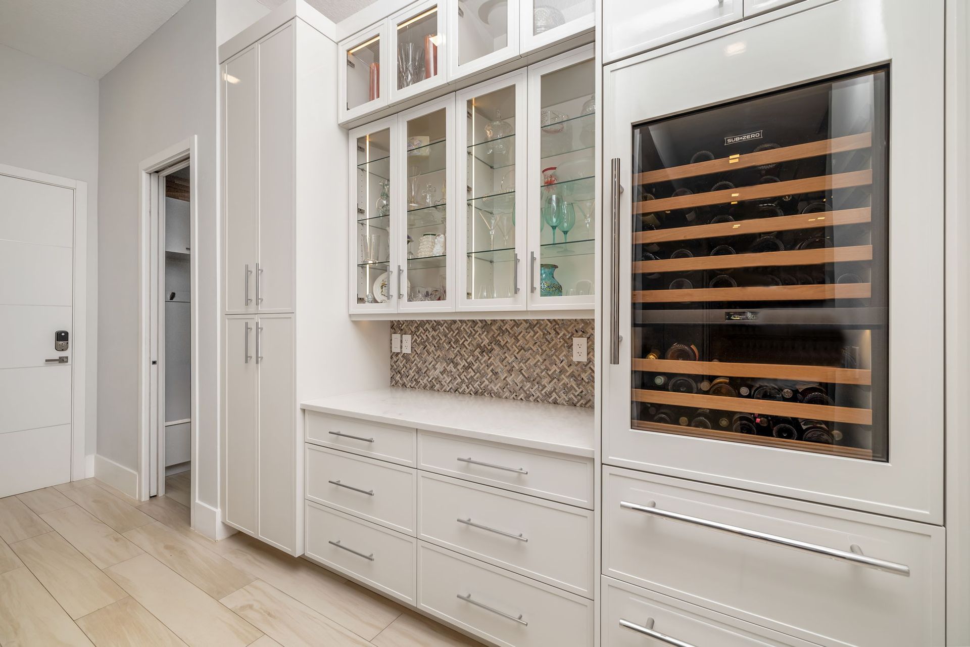 Bright white kitchen with built-in wine cooler, glass cabinets, and light wood floor