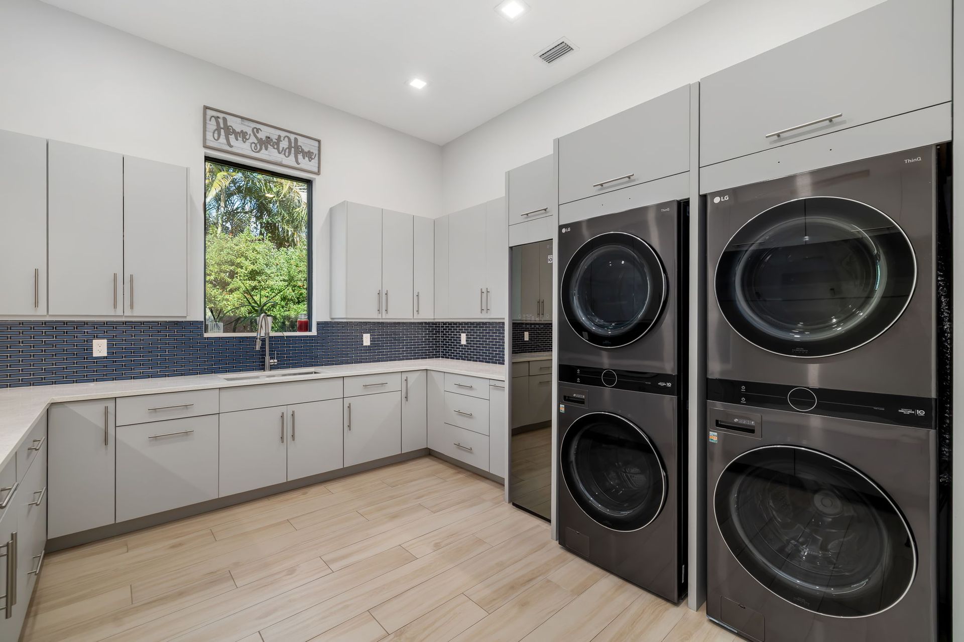 Modern laundry room with white cabinets, blue tile backsplash, and stacked black washer-dryers.