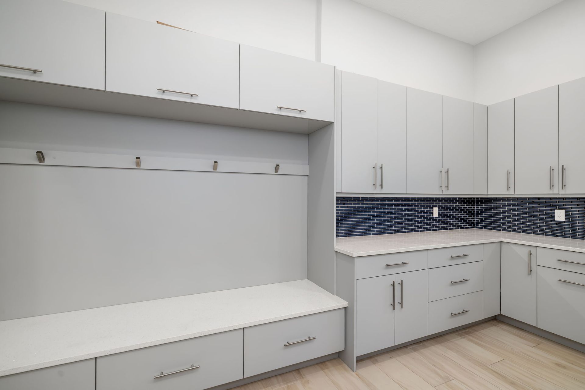 Modern white kitchen with gray cabinets, built-in bench seating, and blue tile backsplash