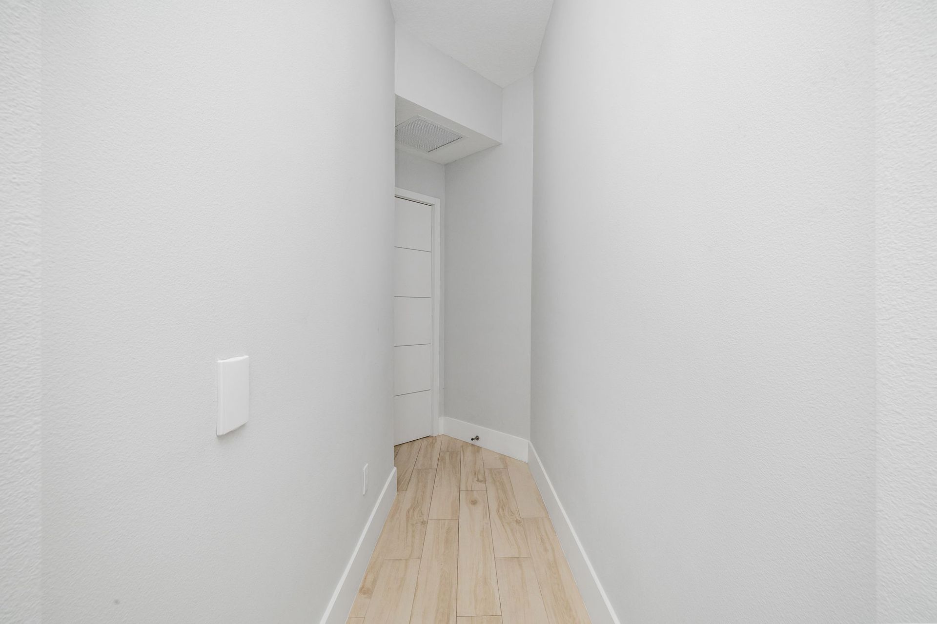 Narrow white hallway with light wood floor and a closet at the end