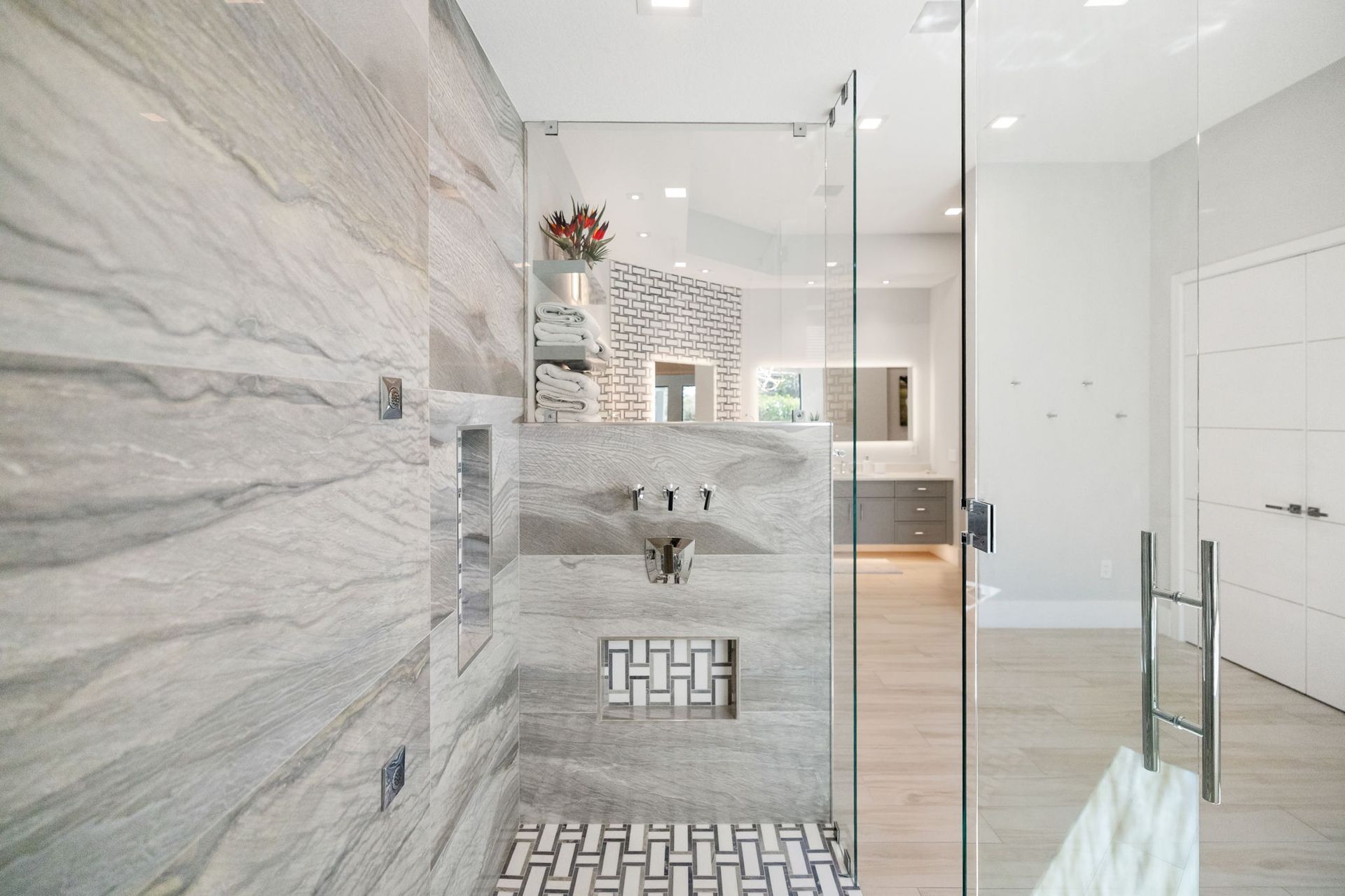 Modern bathroom with glass shower, marble wall, and freestanding tub visible in the background