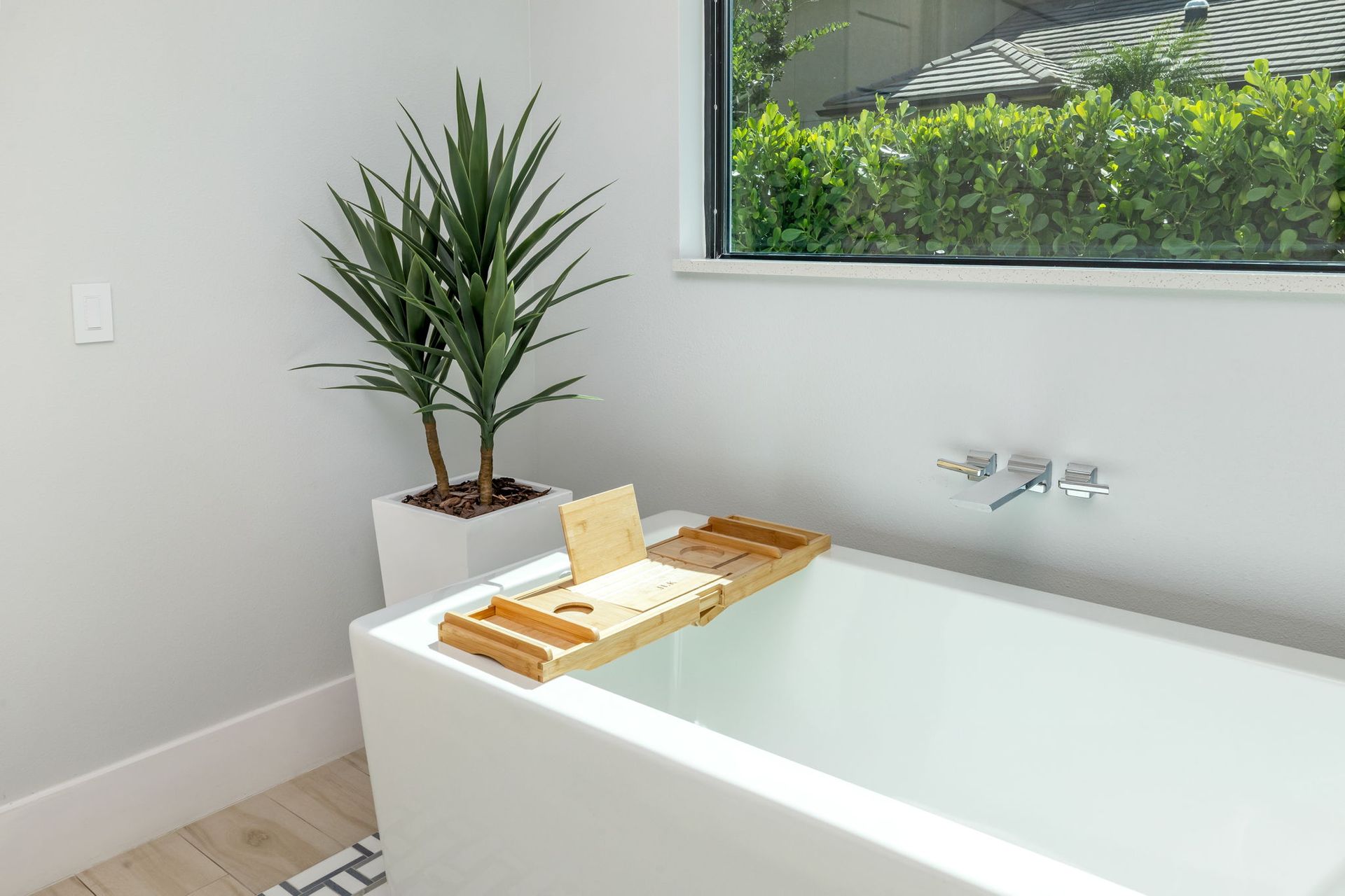 Modern bathroom with white bathtub, potted plant, and tray on the tub edge